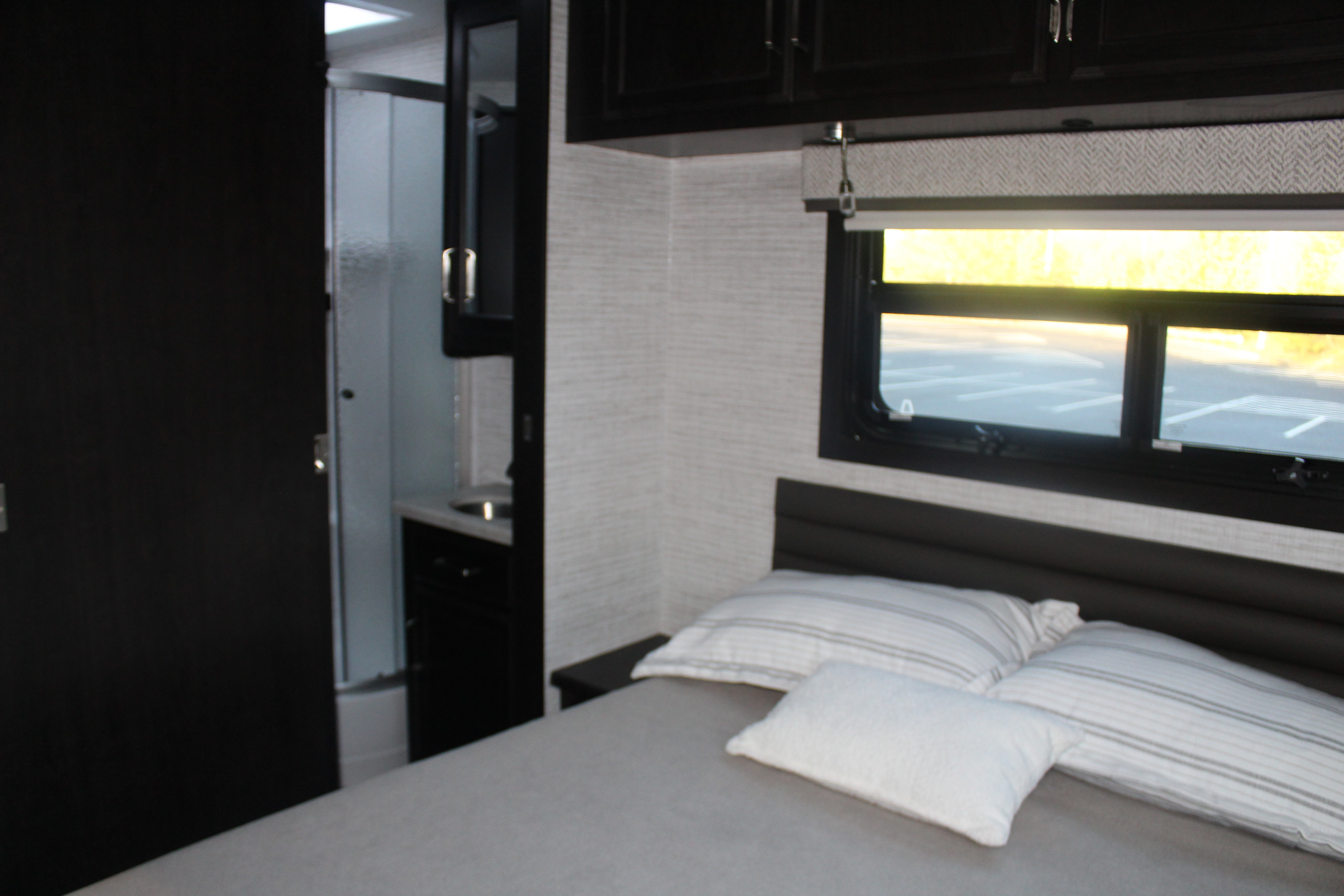 Inside a comfy RV rental: bedroom with a bed, window, cabinets, and a private bathroom with shower.. Entegra Vision 2024