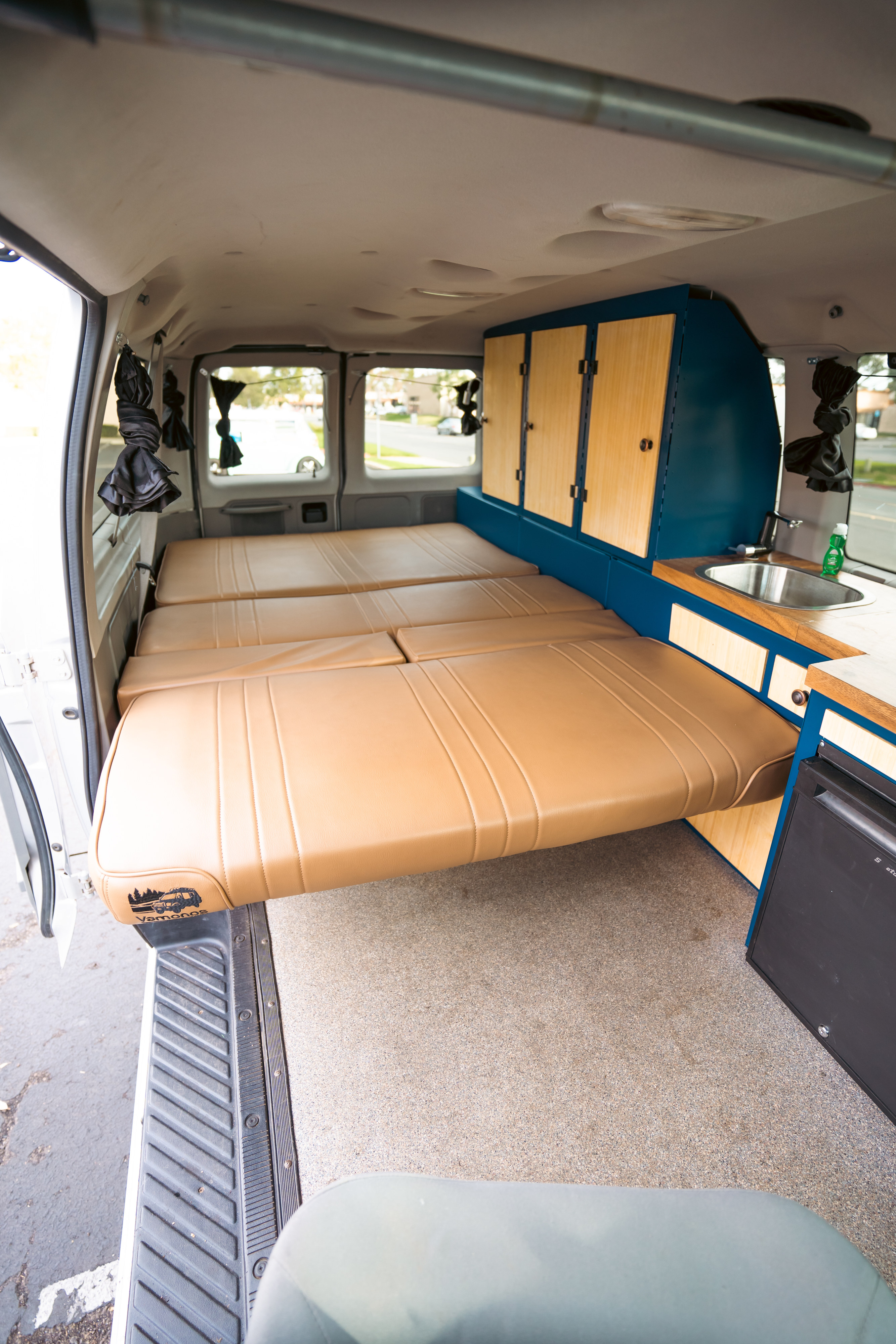 Interior of a camper van RV rental featuring modular beds, a blue and wood kitchenette, and gray carpet flooring.. Ford Ford E350 2008