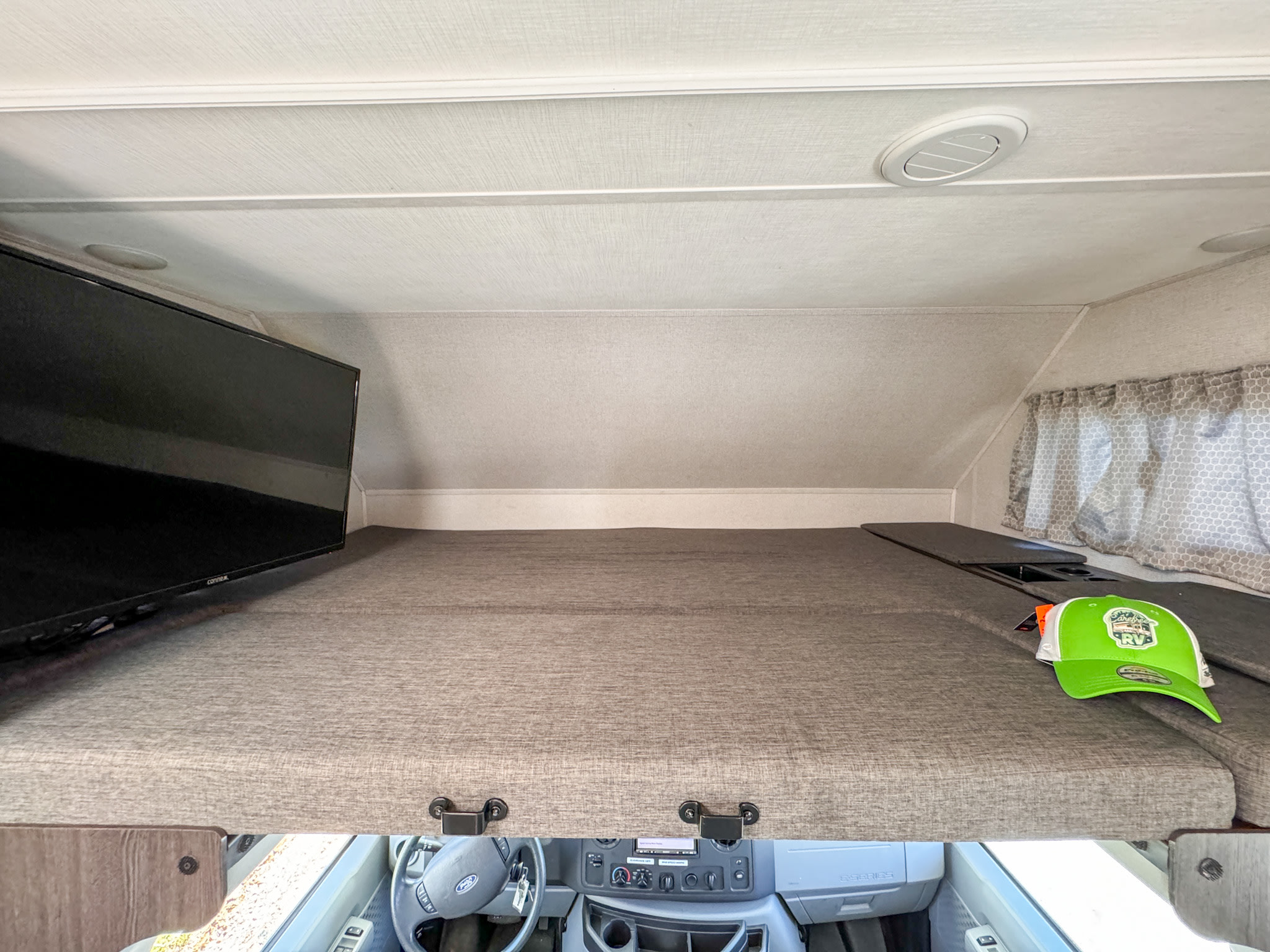 RV rental interior: a spacious cab-over bunk bed with TV, overlooking the Ford dashboard.. Forest River Sunseeker 2021