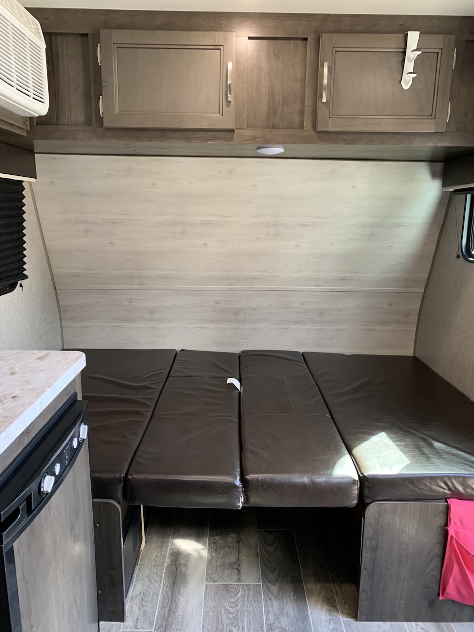 RV rental interior: a comfy dinette converted to a bed, overhead cabinets, and a small counter with a fridge.. Jayco 154BH 2021