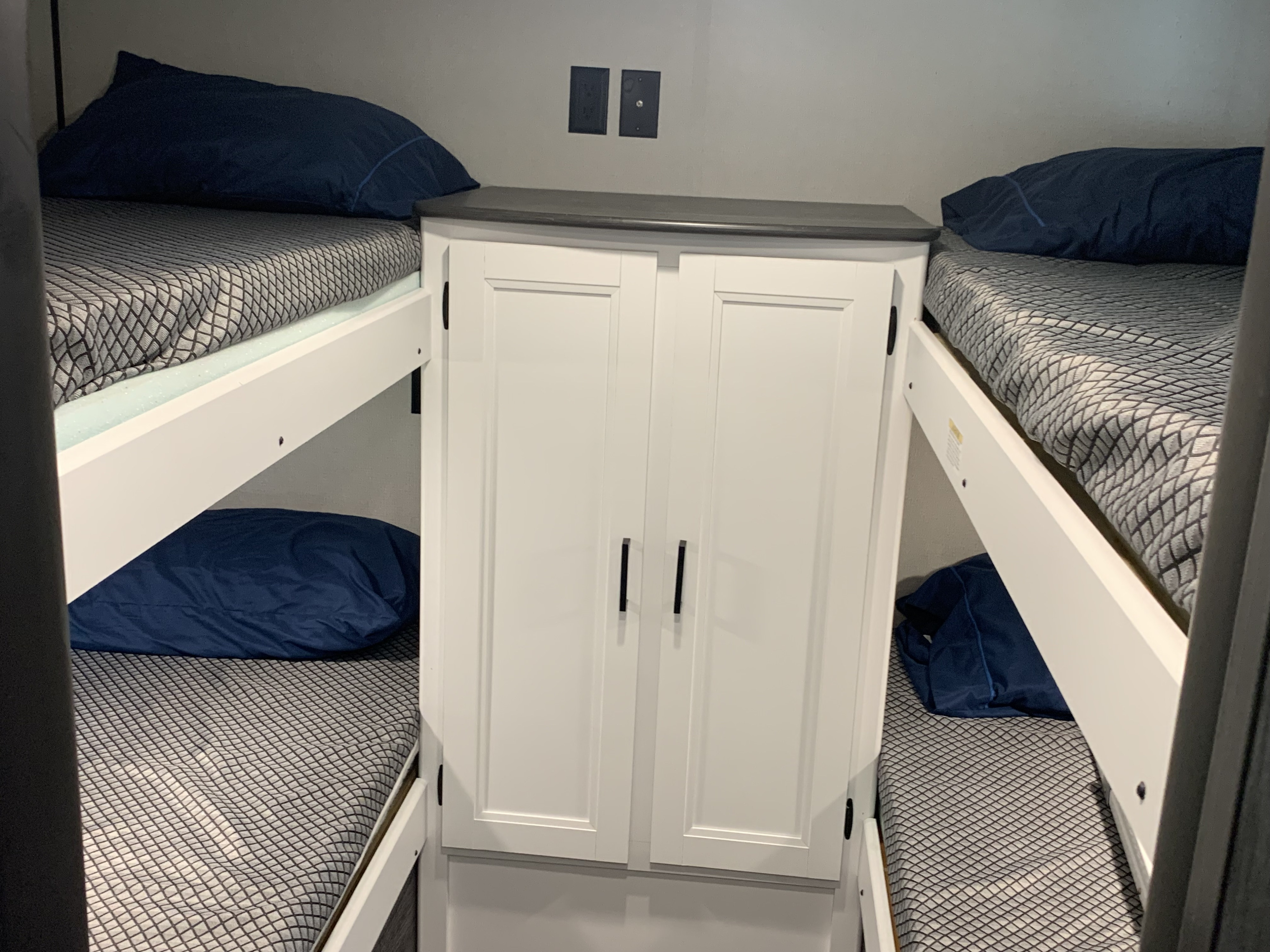 RV rental bunk beds with a central cabinet provide compact sleeping for four. Navy pillows and gray mattresses.. Keystone Hideout 2022