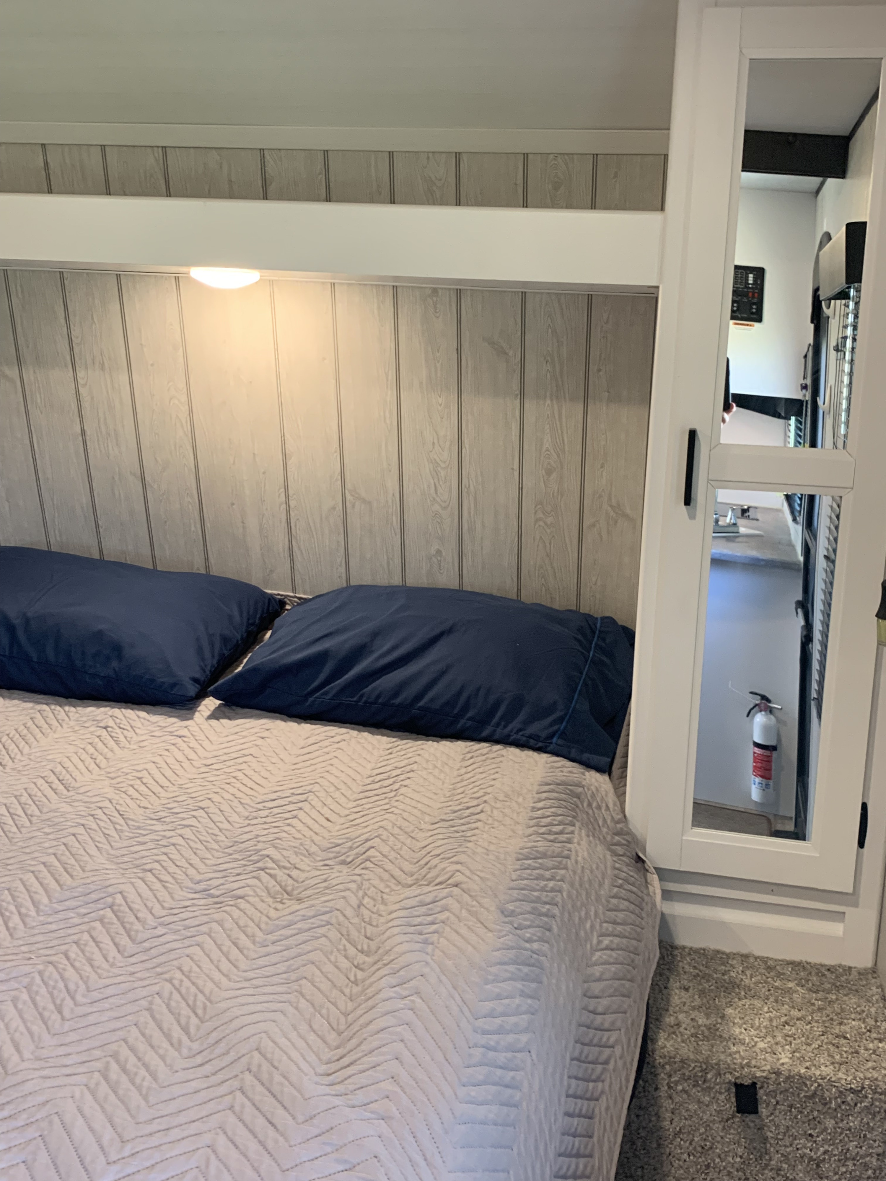 Cozy RV rental bedroom: bed with blue pillows, wood-paneled walls, and mirrored closet. A fire extinguisher is visible in reflection.. Keystone Hideout 2022