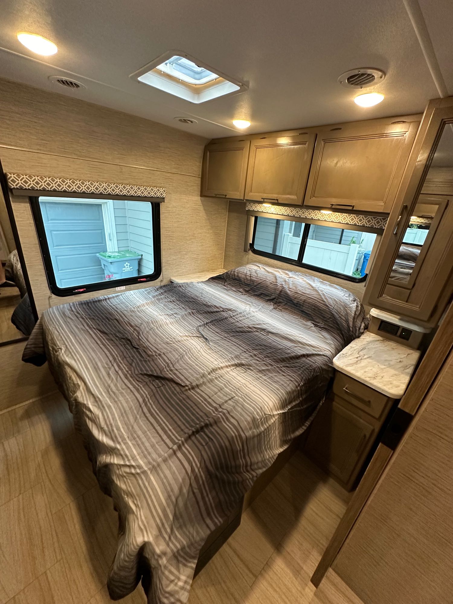 Inside an RV rental: a neat bedroom with striped bedding, windows, storage cabinets, and a skylight.. Thor Coleman 2022
