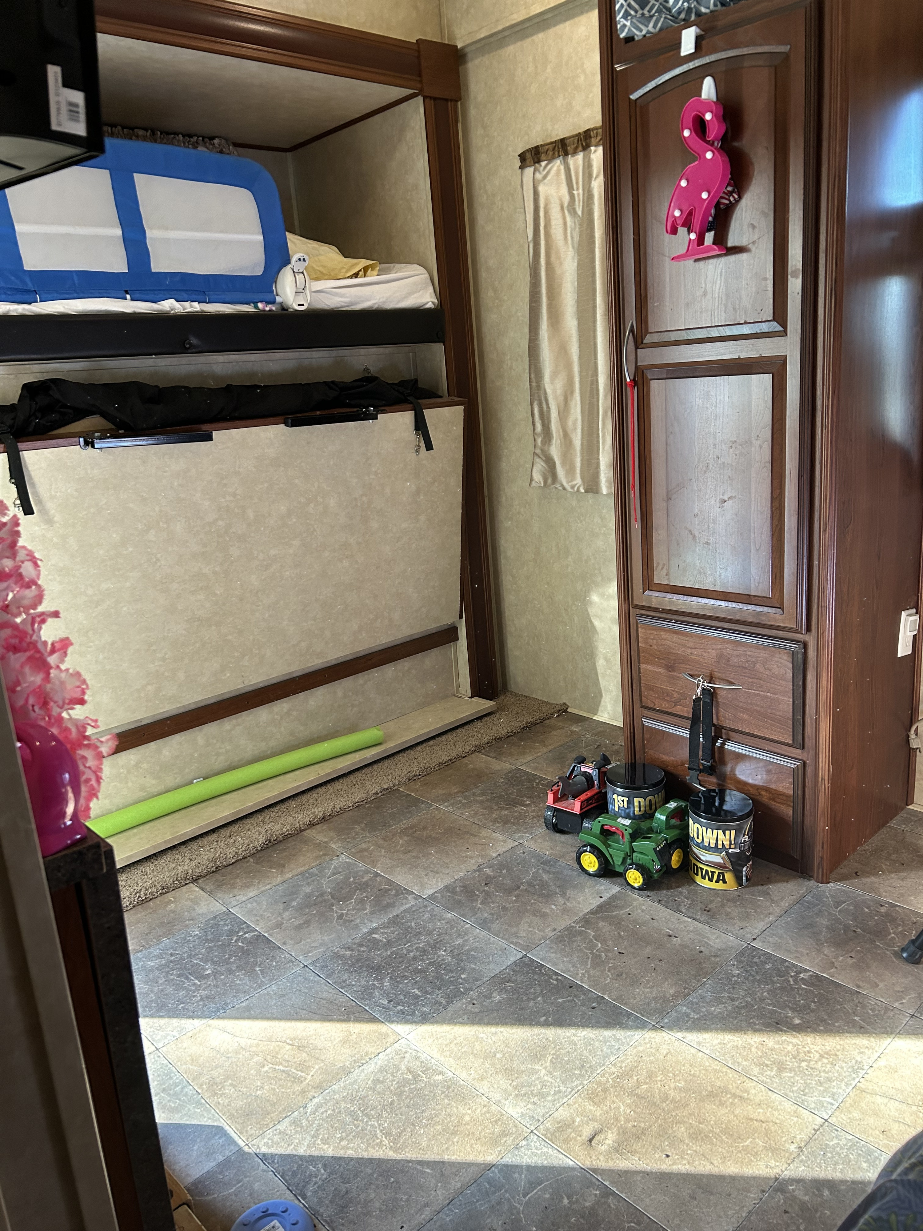 Inside an RV rental: bunk beds with a blue safety rail, a fold-up lower bed, wooden cabinets, and kids' toys on the tiled floor.. Palomino Columbus 2015