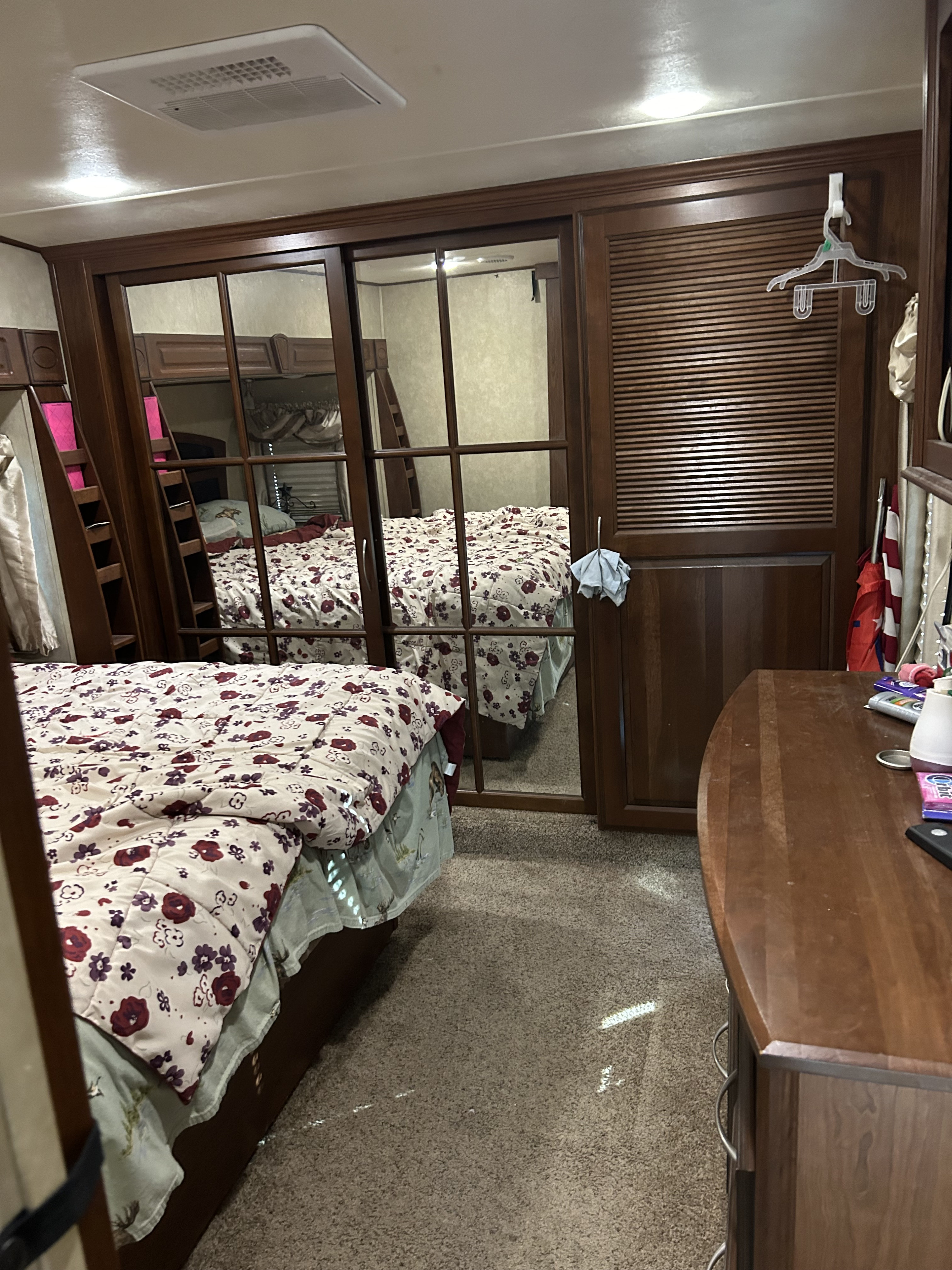 Inside an RV rental: a cozy bedroom with floral comforter, mirrored closet reflecting a bunk, and ceiling AC.. Palomino Columbus 2015