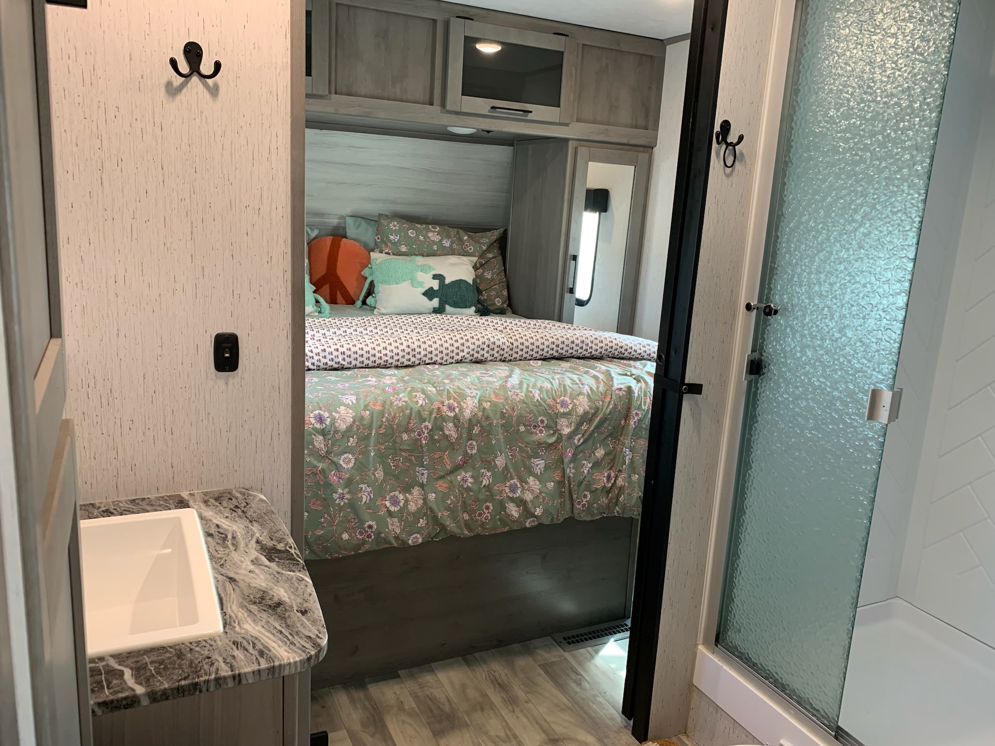 Inside an RV rental: view of a bedroom with floral bed, an adjacent sink, and a frosted glass shower stall.. Dutchmen Kodiak Ultra Lite 2022