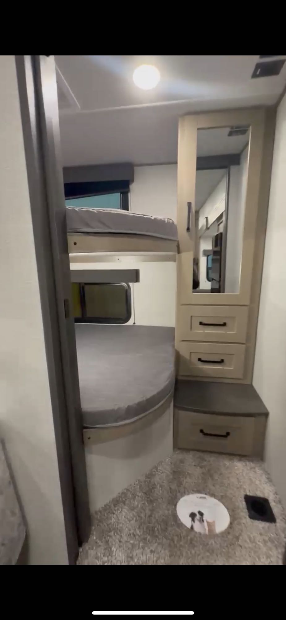 Cozy RV rental interior featuring bunk beds, a storage cabinet with a mirror, and soft carpet. A round mat with animal images sits on the floor.. Grand Design Reflection 100 27BH 2024