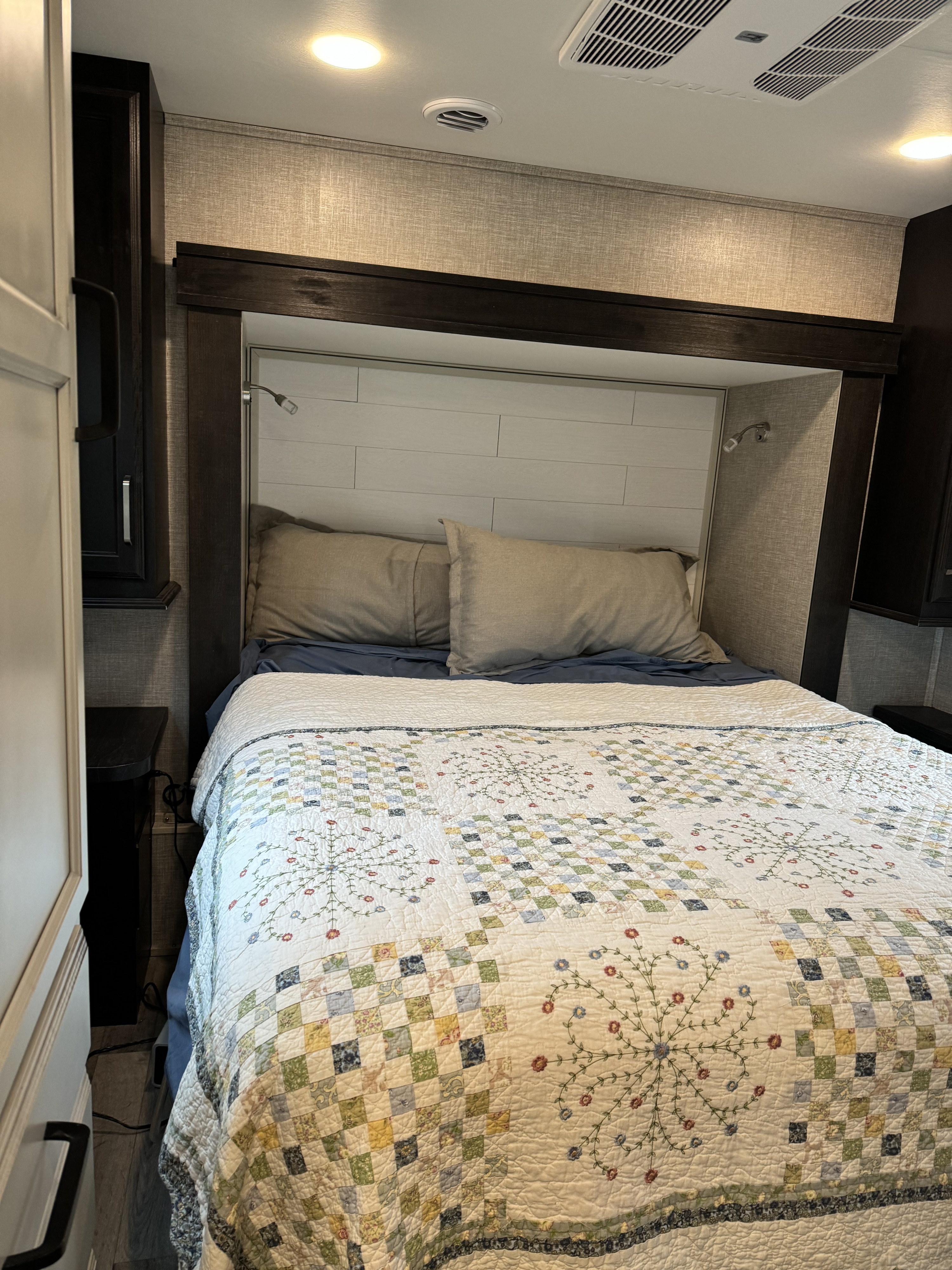 A comfortable bed in an RV rental, featuring a colorful quilt, reading lights, and an overhead AC vent. Ideal for travel.. Entegra Coach Odyssey 2022
