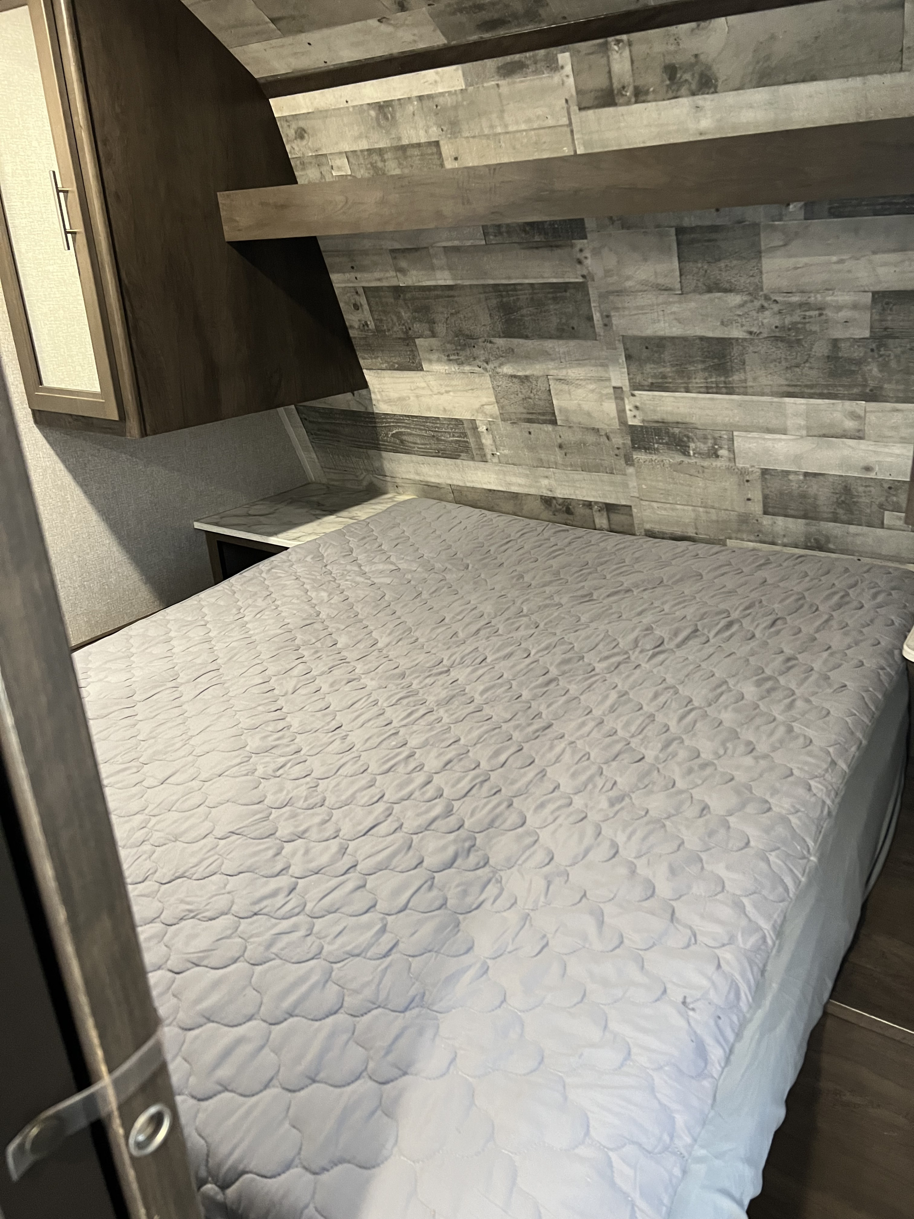 Cozy RV rental bedroom with a grey quilted bed, distressed wood paneling, and practical storage cabinets. A compact and functional space.. Coleman Lantern 2021