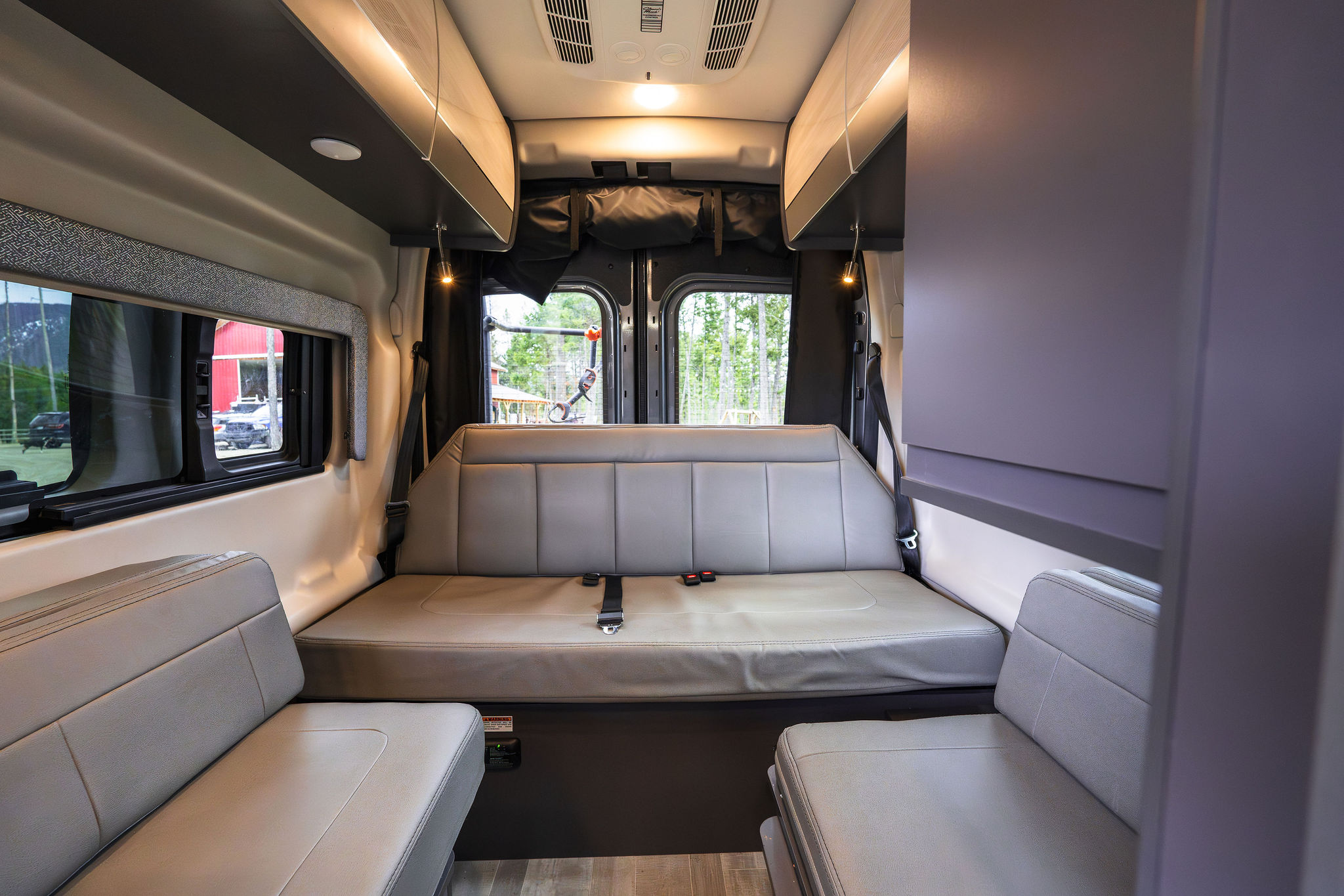 Spacious RV rental interior with comfortable light-grey seating & convertible bed in a modern camper van.. Thor Sanctuary 2023