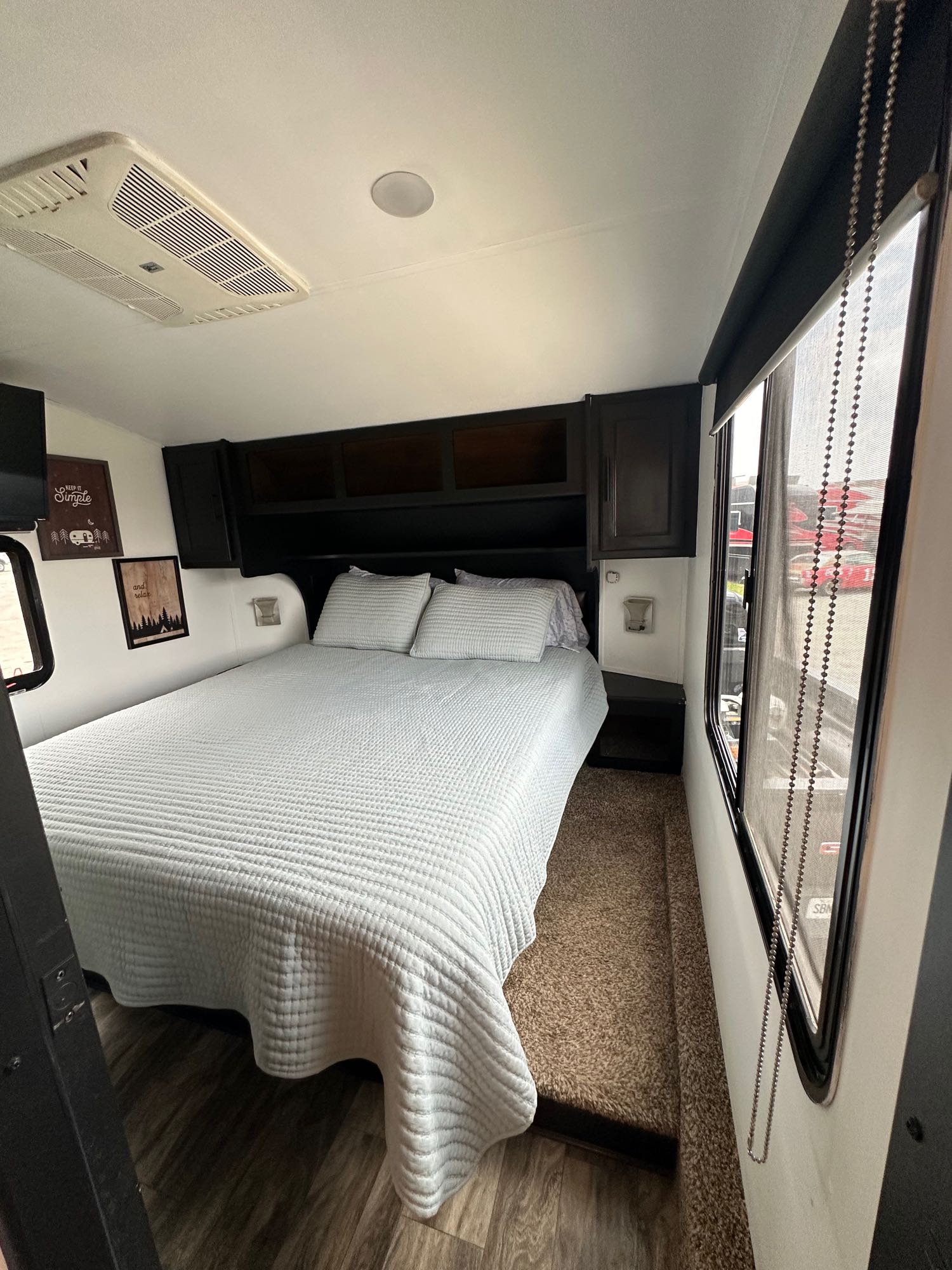 Comfortable RV rental bedroom featuring a bed with light bedding, ceiling AC, built-in storage, and a side window.. Grand Design Reflection 2019