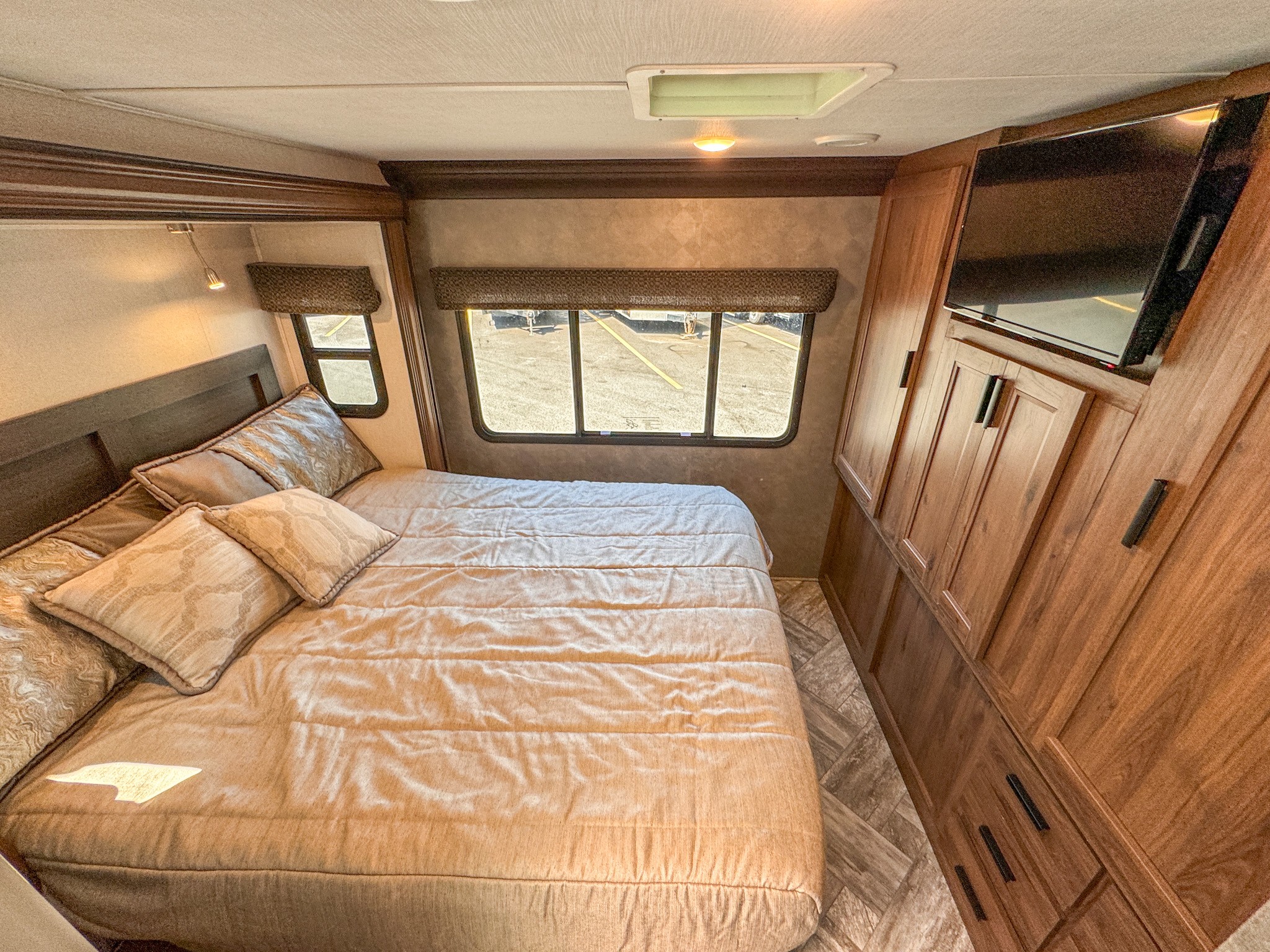 Comfortable RV bedroom interior, perfect for your next RV rental. Features a cozy bed, mounted TV, and stylish wood cabinetry.. Forest River Sunseeker 2021