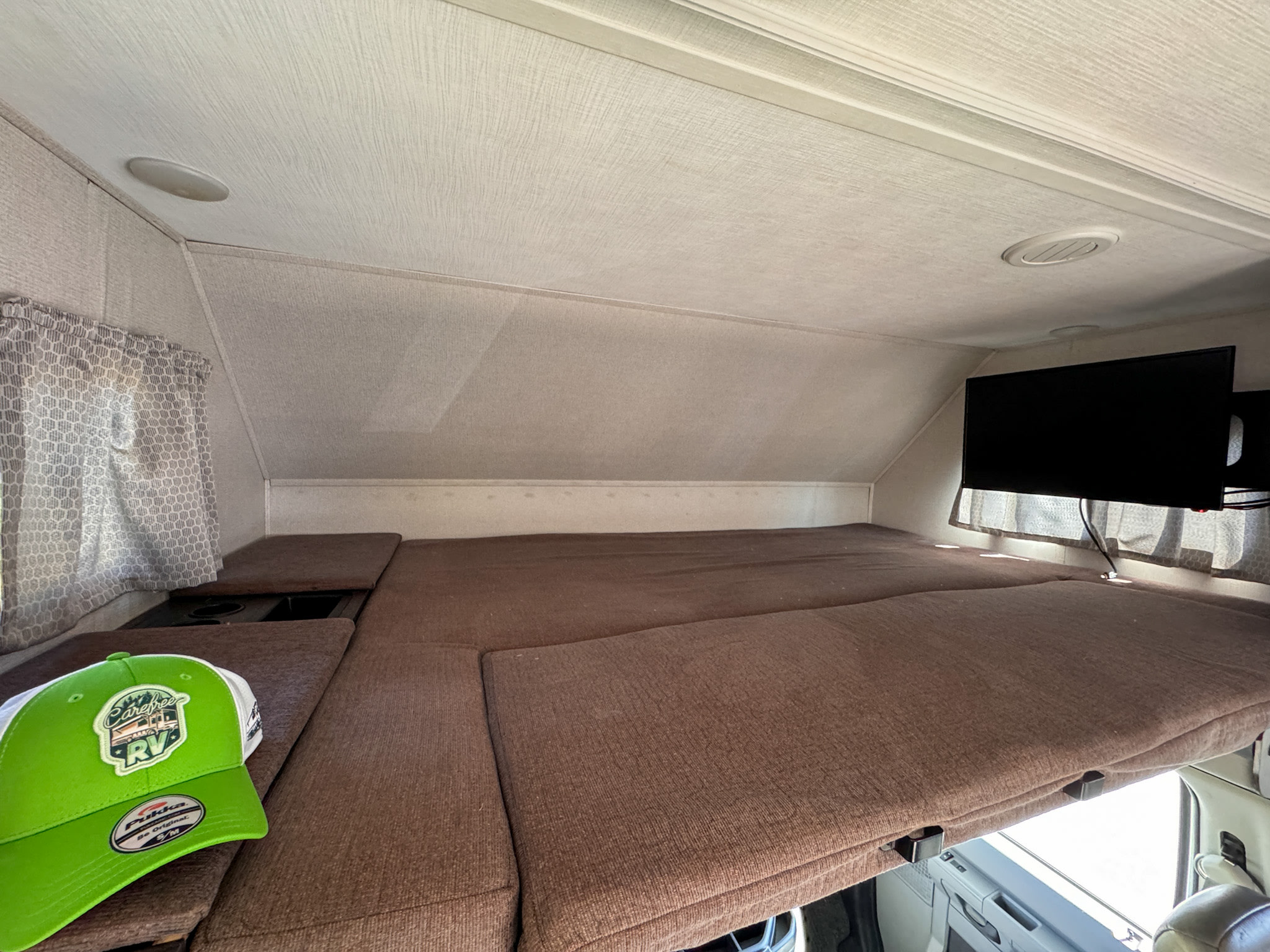 Cozy over-cab bunk bed in an RV rental, featuring a TV and window. Ideal sleeping space for your camper adventures.. Forest River Sunseeker 2022