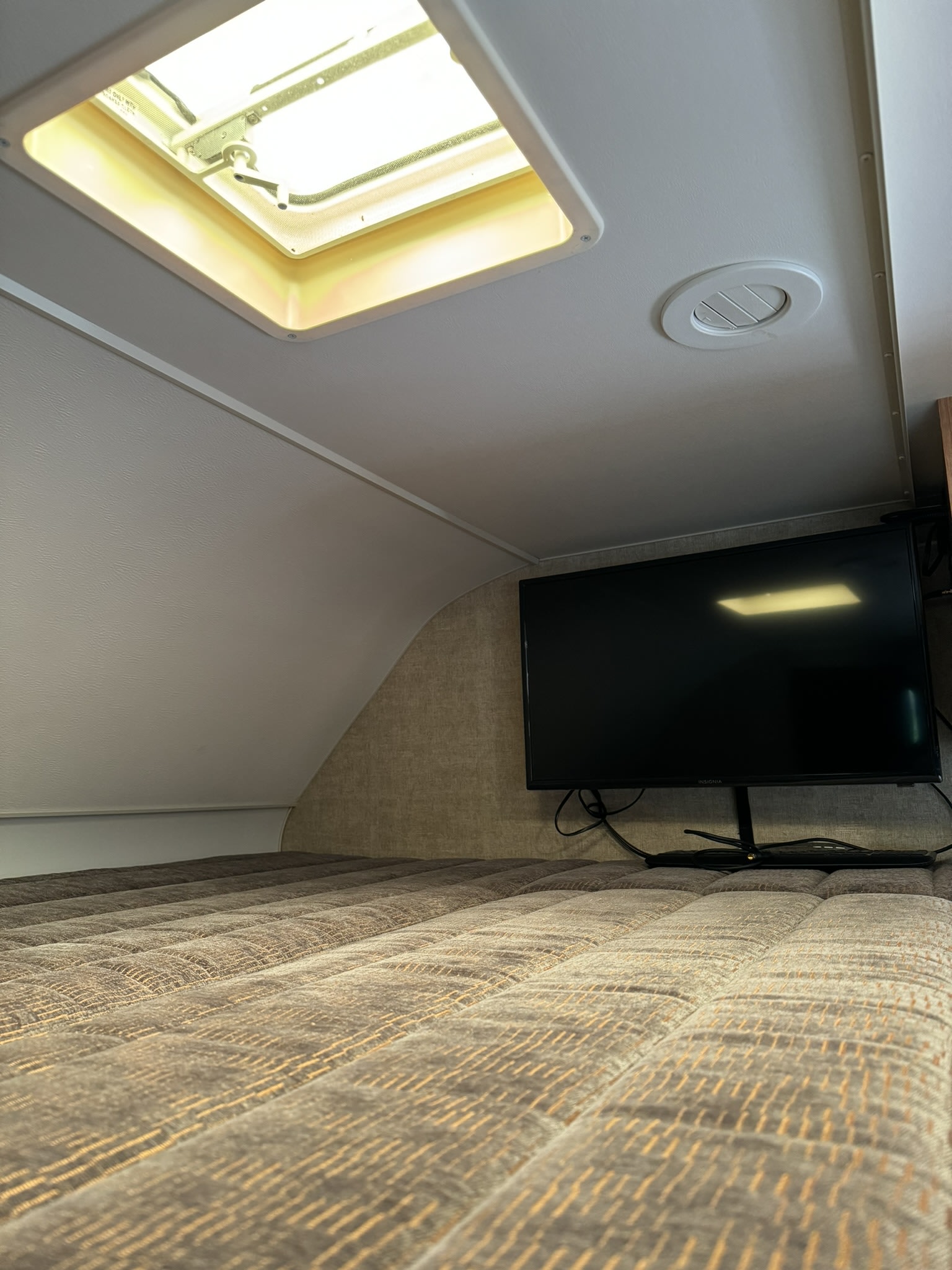 RV rental interior showing a comfortable bed, flat-screen TV, ceiling vent, and bright skylight above the sleeping area.. Winnebago Minnie Winnie 2018