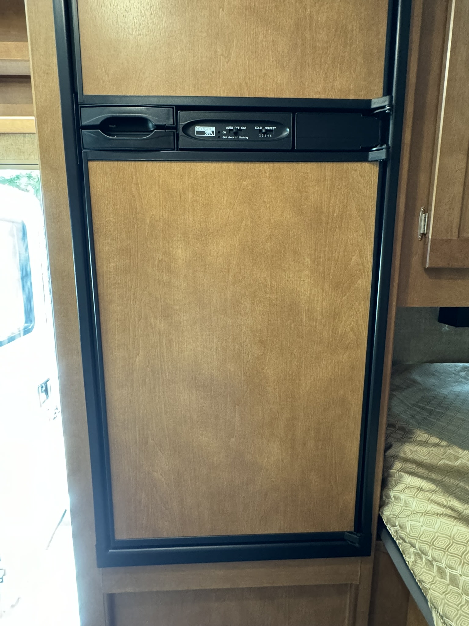 Wood-paneled Norcold RV refrigerator in an RV rental. A compact appliance visible inside the vehicle, near a window.. Winnebago Minnie Winnie 2018