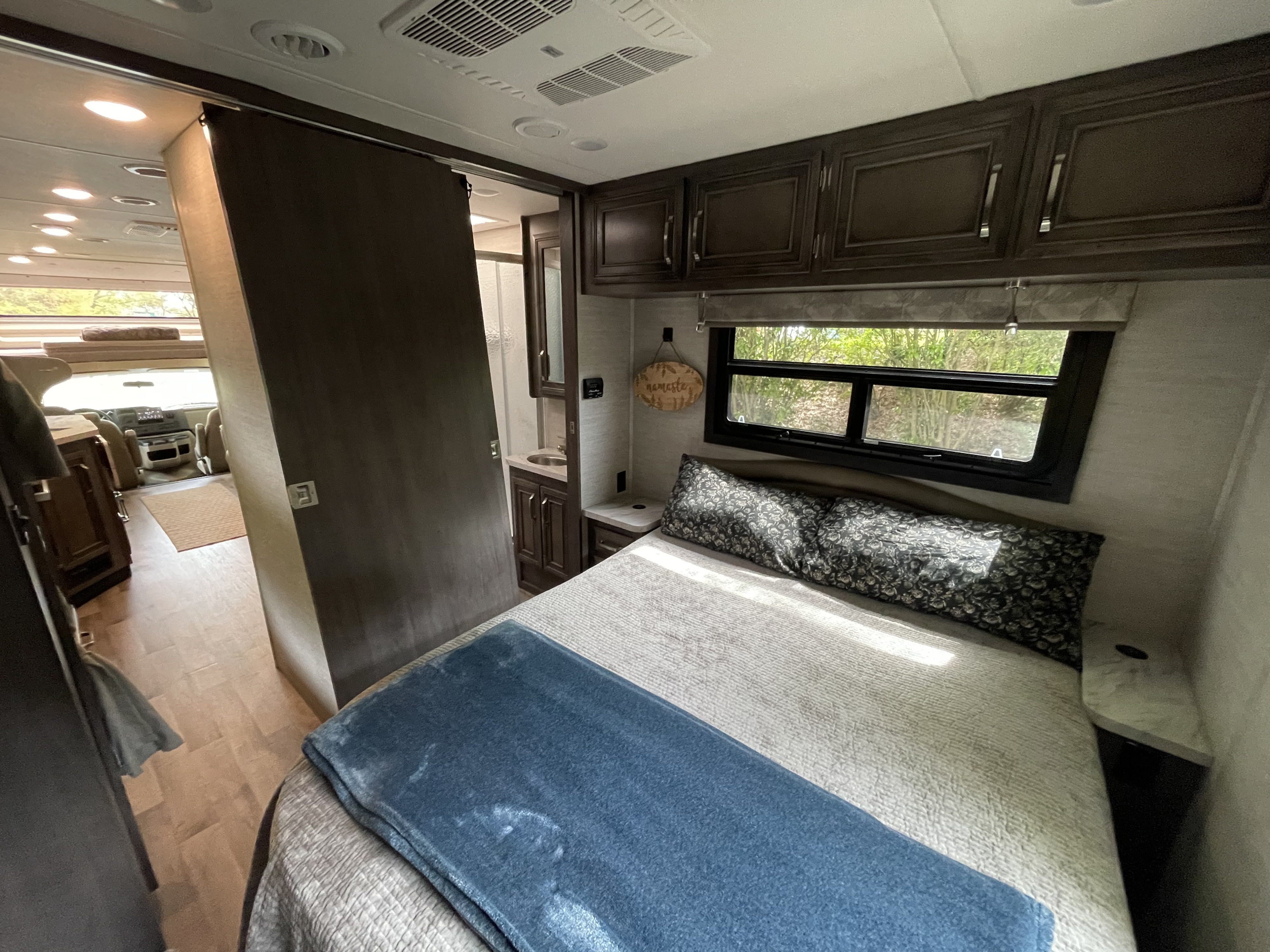 Cozy RV rental interior: a bedroom with bed & window, leading to a compact bath & driver's area. Ideal for travel.. Jayco Greyhawk 2023
