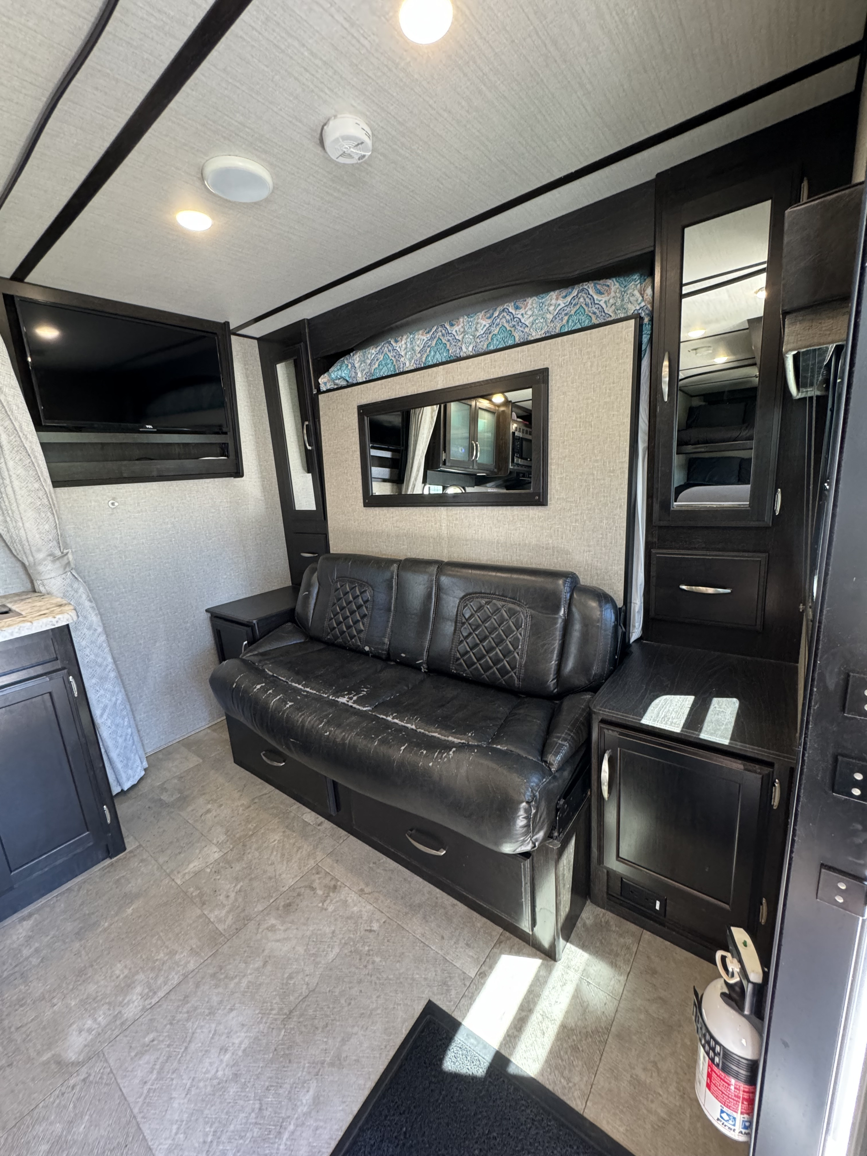 RV rental: The spacious living area features a black leather sofa, wall-mounted TV, an overhead bunk, and built-in storage.. Grand Design Imagine 2019