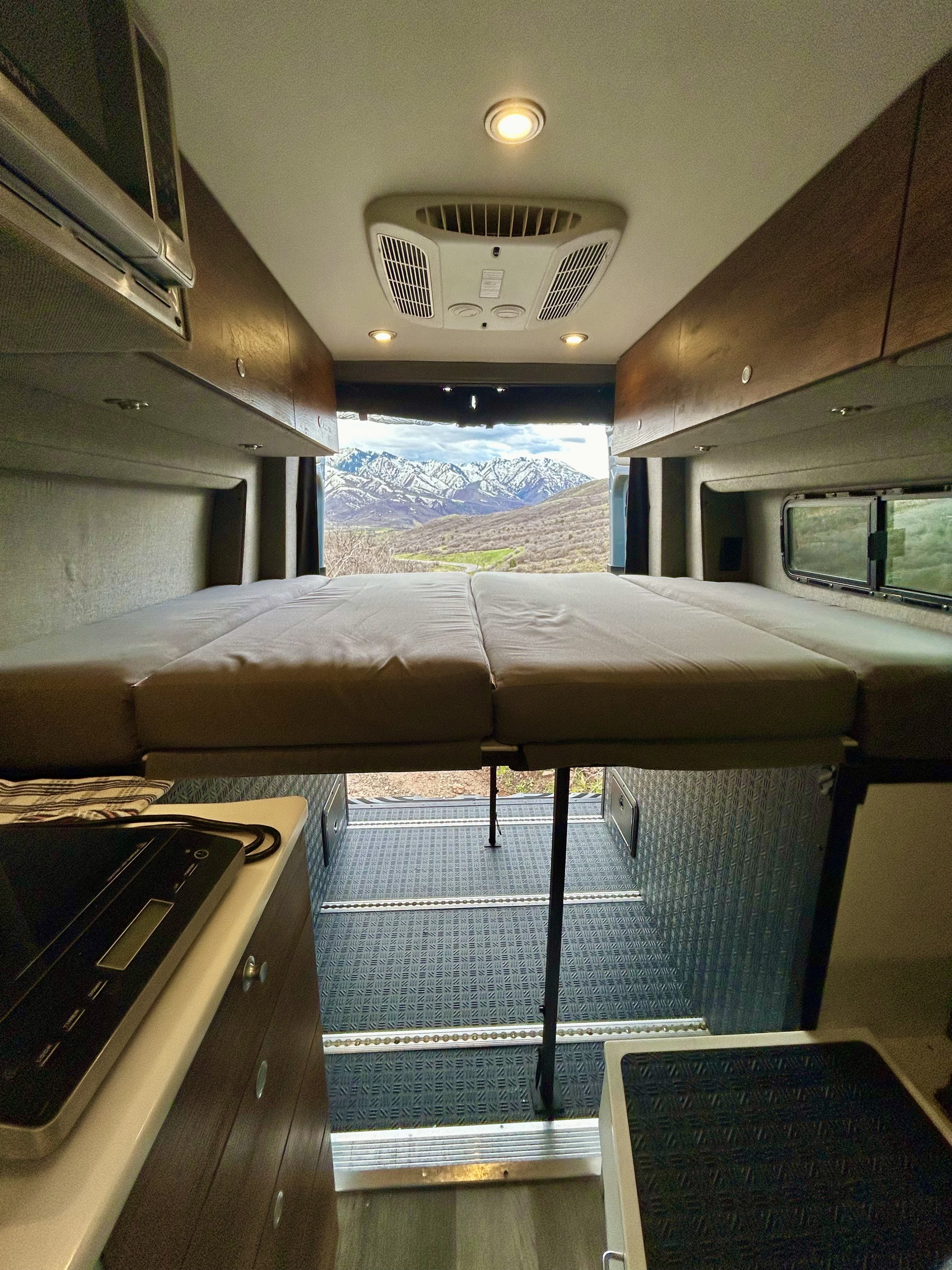 RV rental interior: raised bed with mountain view from back, overhead AC, and kitchenette area.. Storyteller Overland Storyteller Overland Class B 2021
