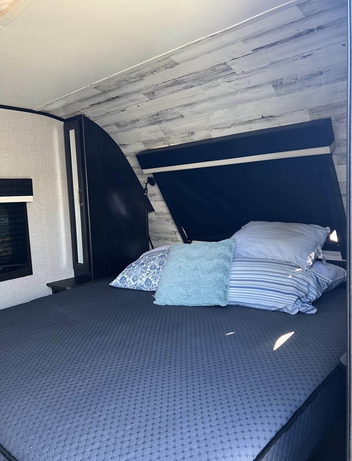 Cozy RV rental bedroom featuring a large bed with blue and striped pillows, textured walls, and black trim for a comfortable stay.. Jayco White Hawk 2021