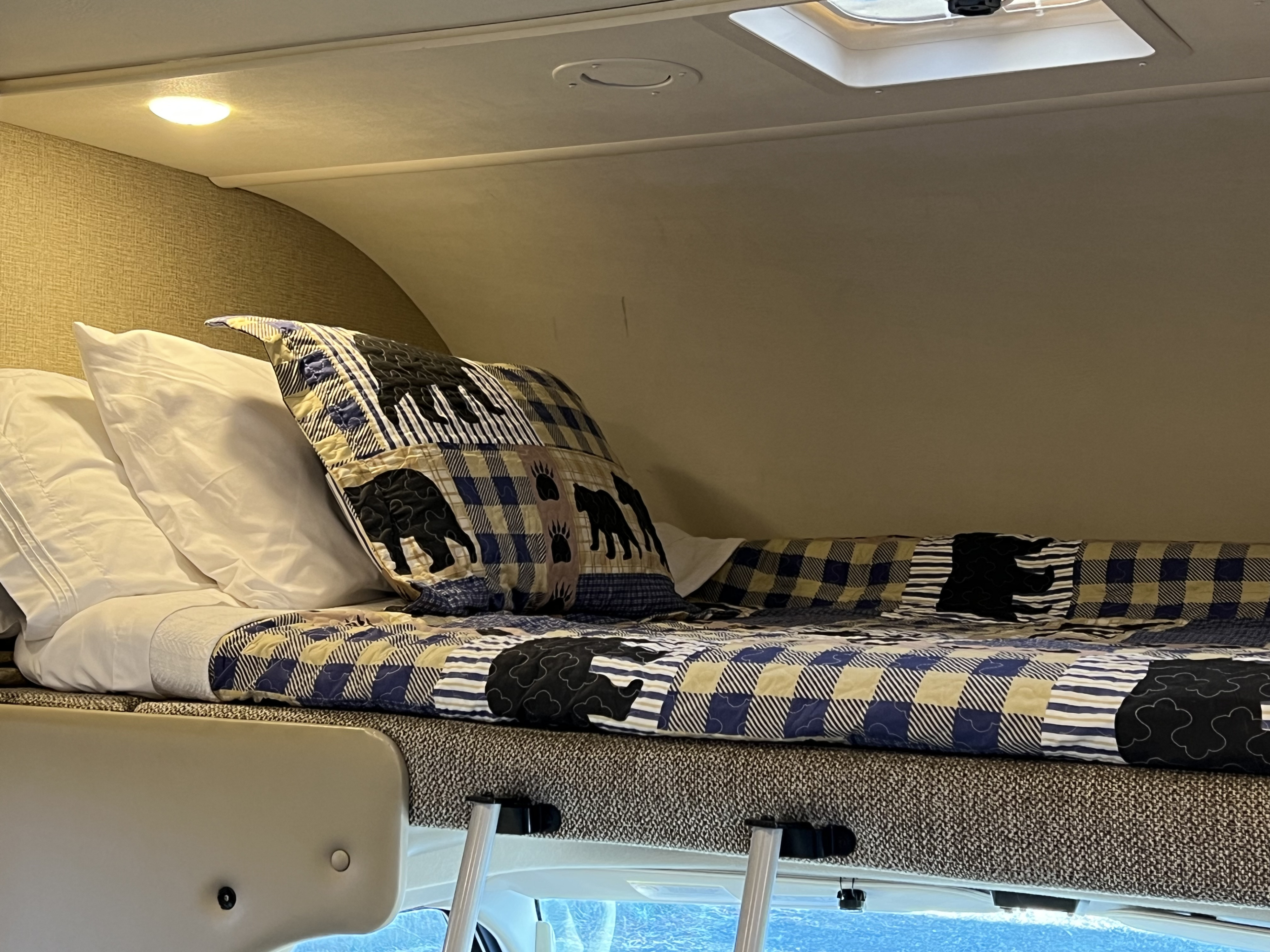 Over-cab RV rental bunk with bear-patterned quilt and pillows, showing interior comfort.. Thor Chateau 2019