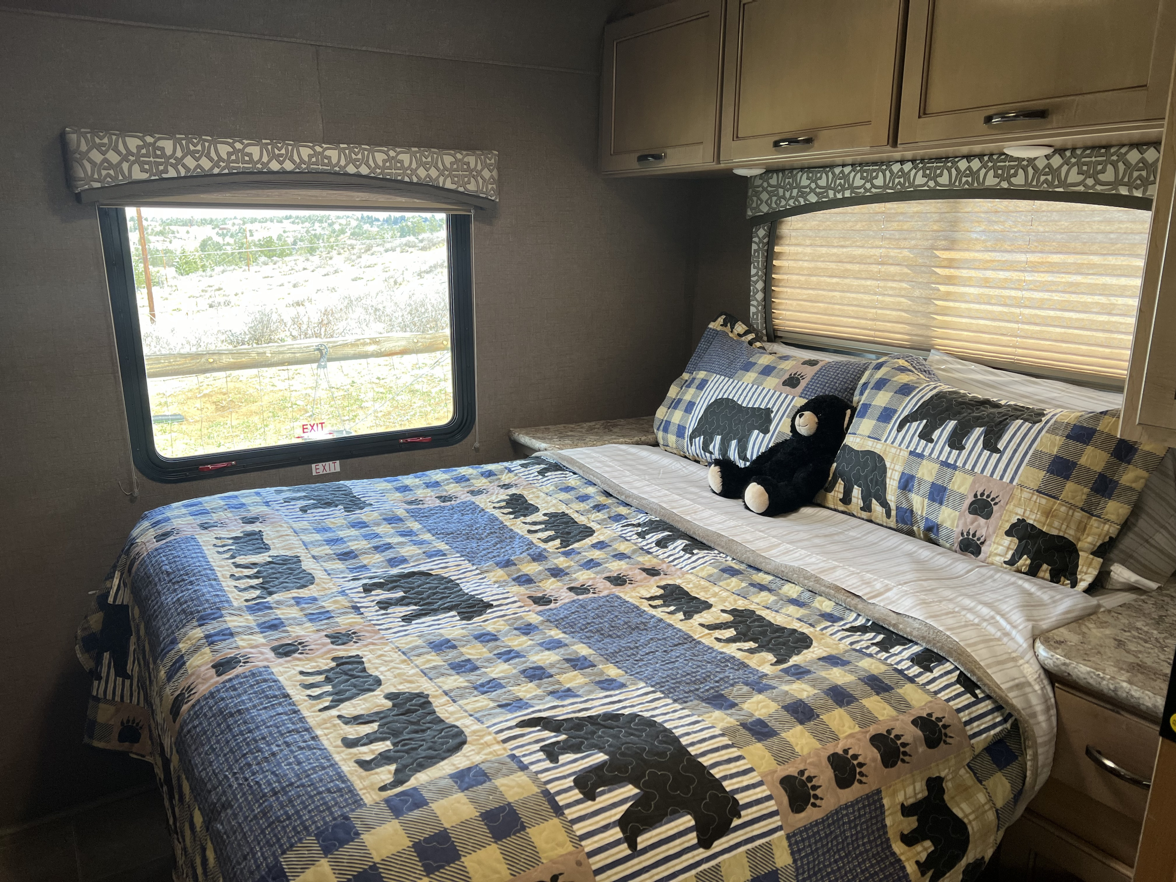 Cozy RV rental bedroom featuring a bear-themed bed, patterned valances, and overhead cabinets. Relaxing for travel.. Thor Chateau 2019