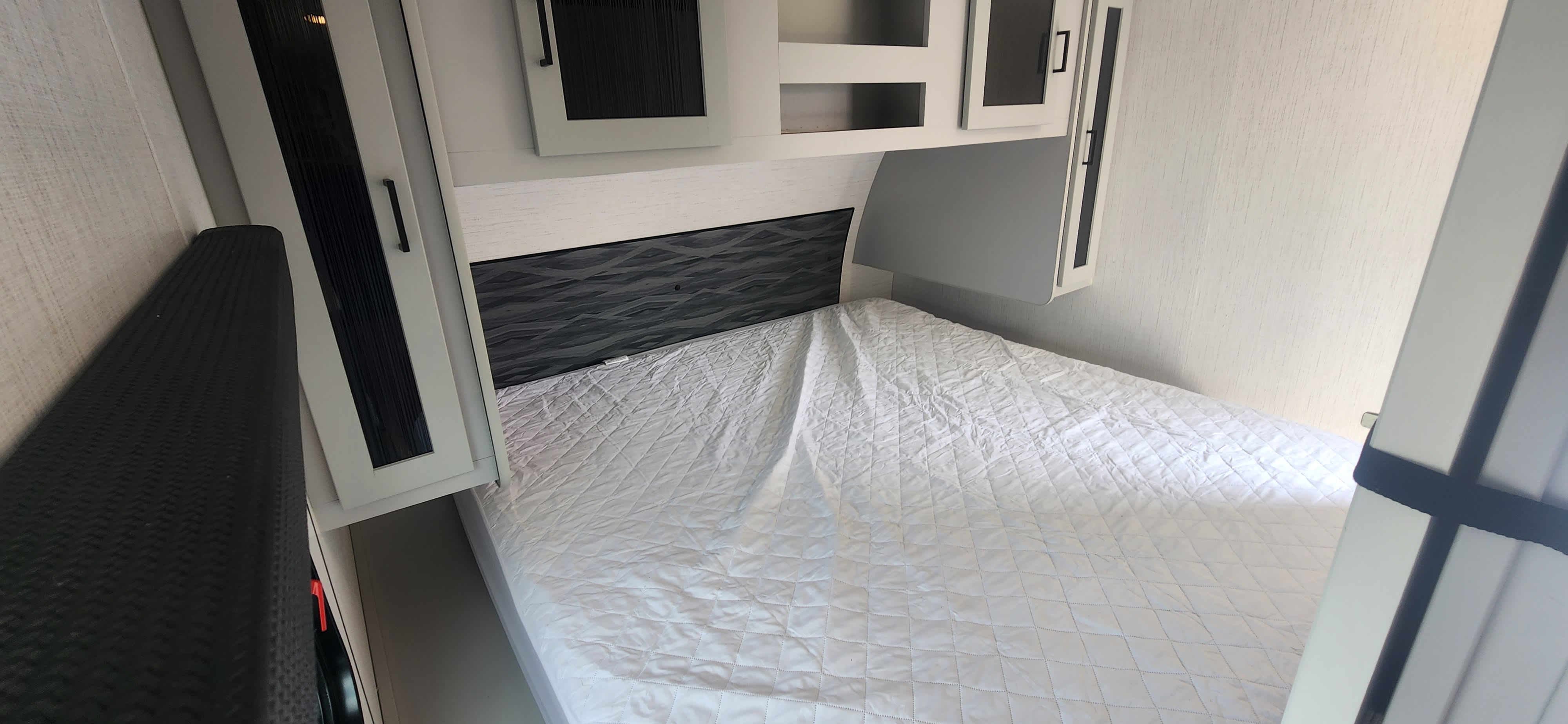 Cozy RV rental bedroom with a comfy bed, modern headboard, and overhead storage cabinets for your travels.. Heartland North Trail 2022