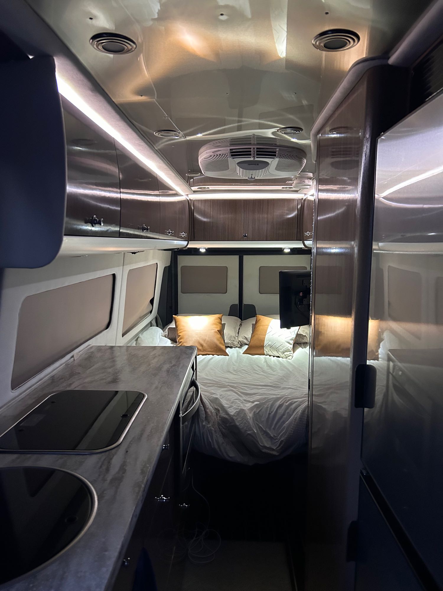 Modern rv rental camper van interior with kitchen, bed, and overhead cabinets.. Airstream Interstate 2017