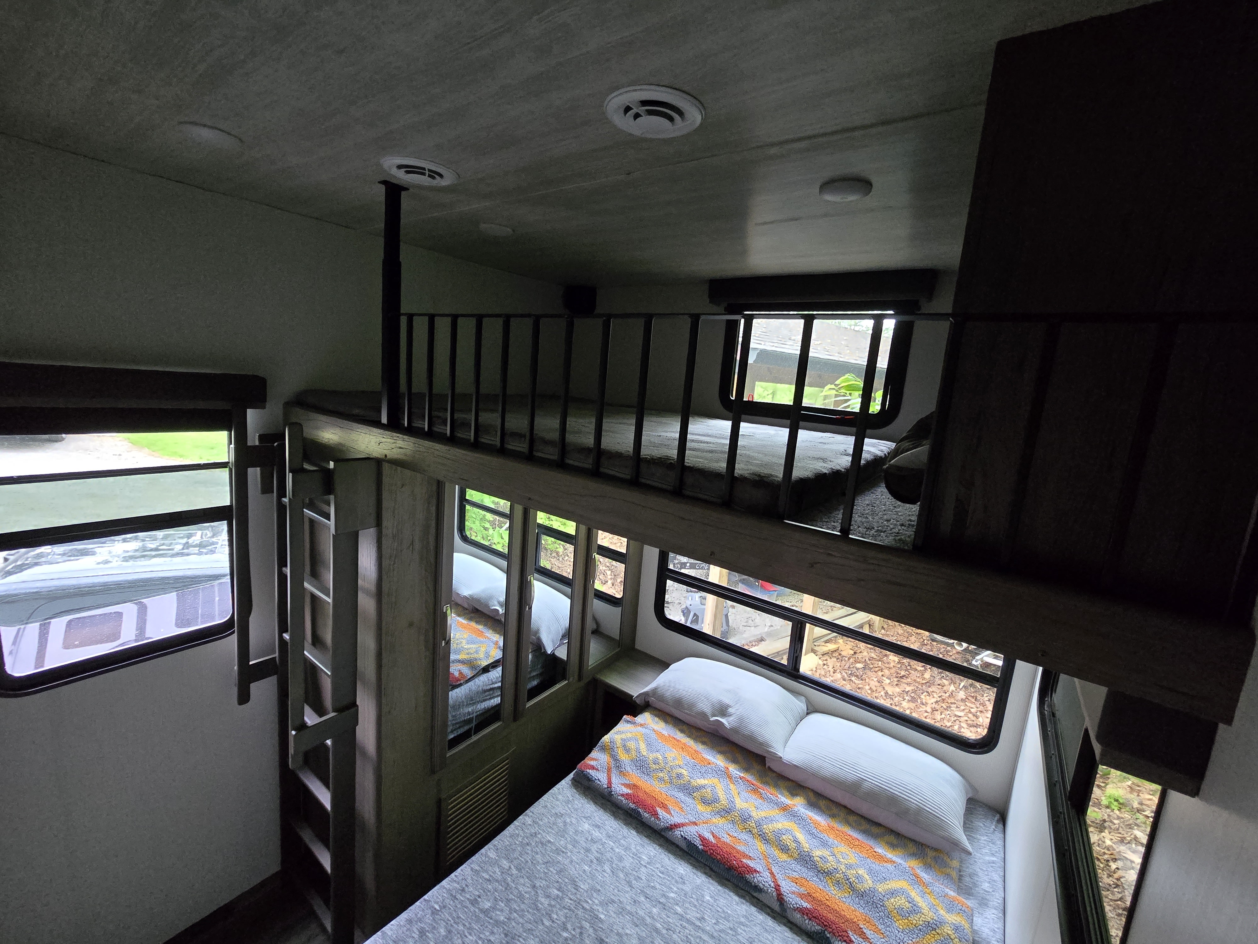 Spacious RV rental with lower bed, colorful blanket, and upper bunk with ladder and railing.. Keystone RV Cougar 2023