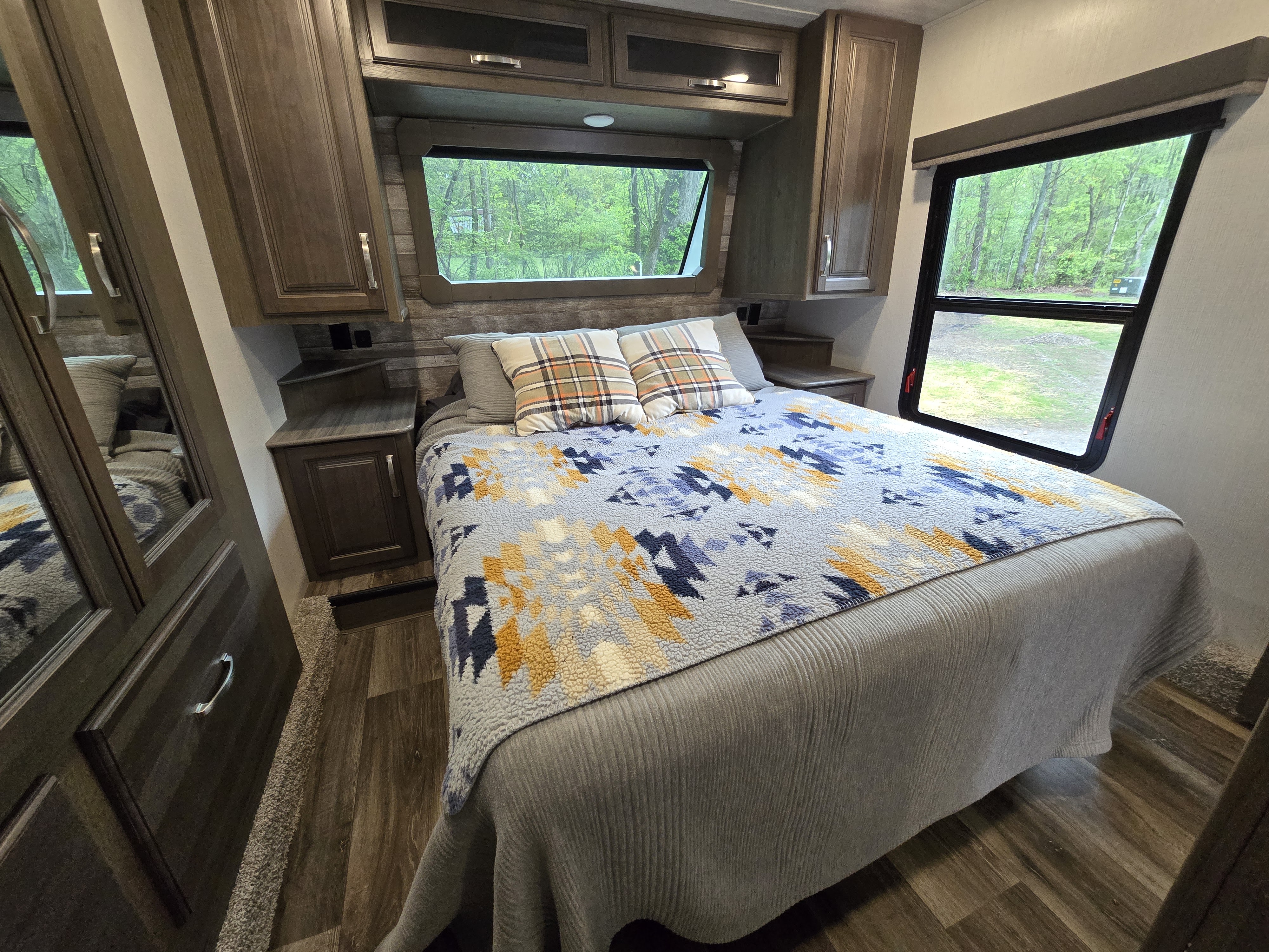 Cozy RV rental bedroom with patterned bedding, built-in cabinets, and window views of nature.. Keystone RV Cougar 2023
