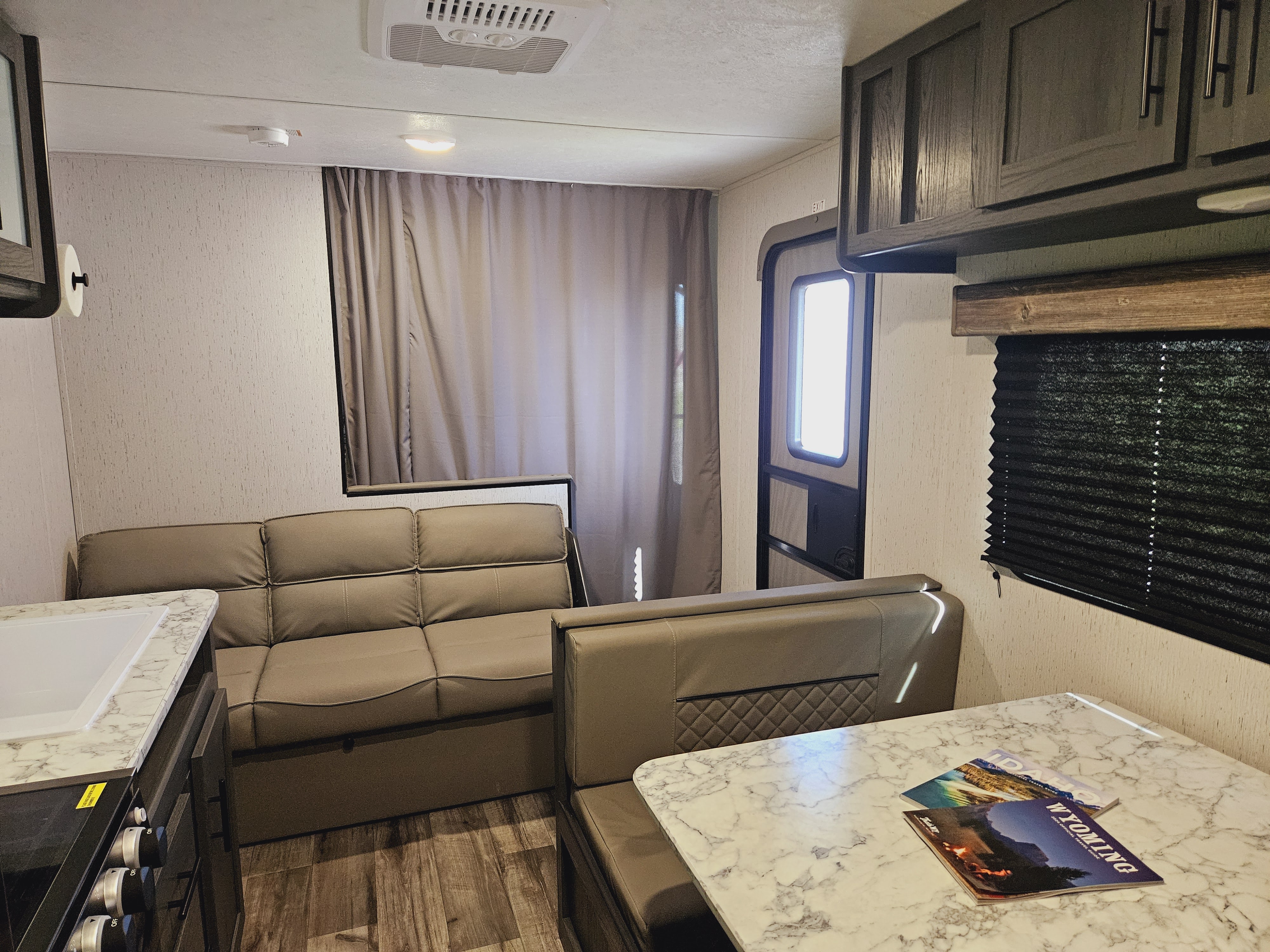 Modern RV rental interior: dinette with travel guides, comfortable sofa, and compact kitchen. Perfect for your next adventure!. Dutchmen TT 2024