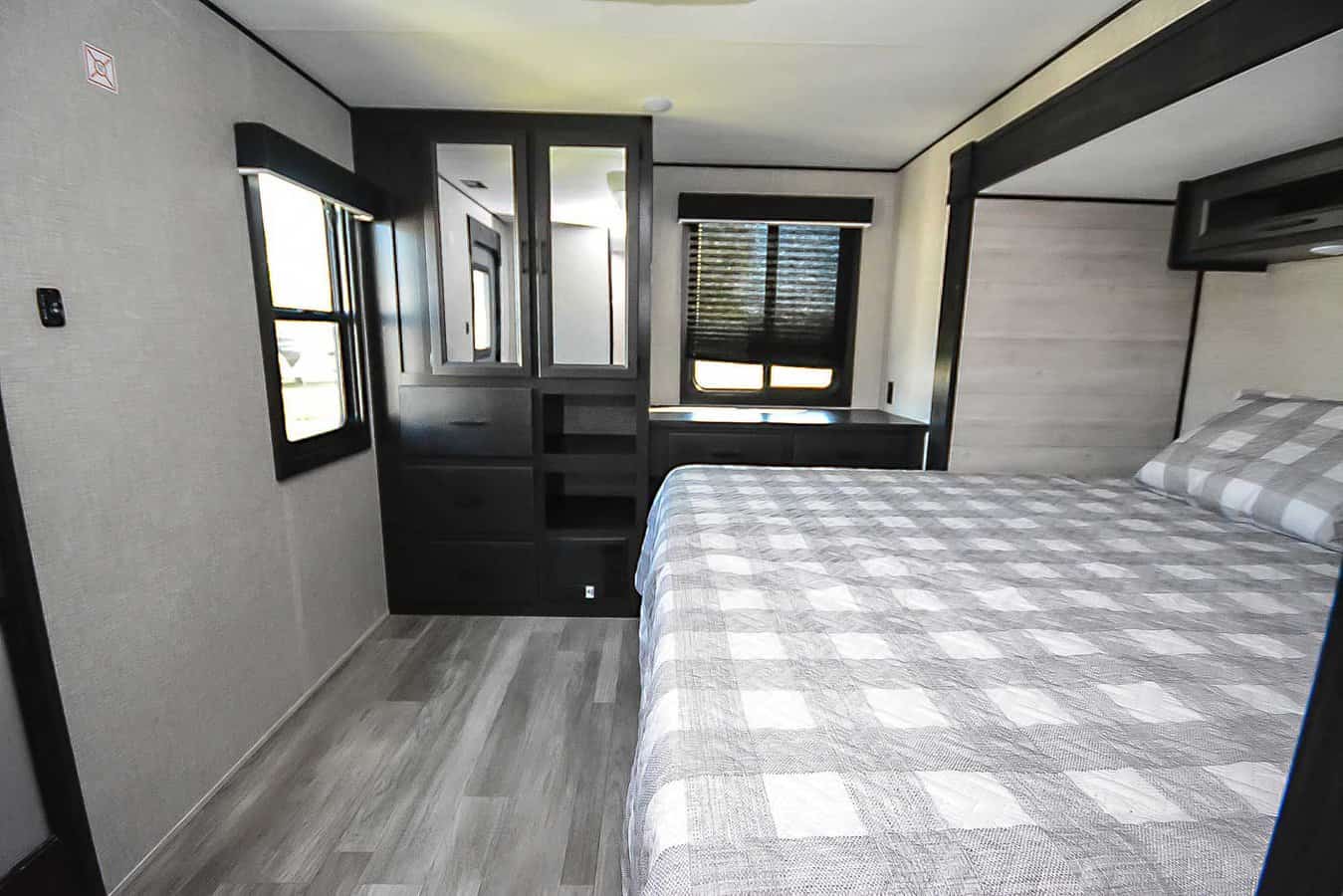 RV rental interior showing a bedroom with a checkered bed, built-in mirrored wardrobe, and windows for natural light.. Jayco Jay Flight 2023