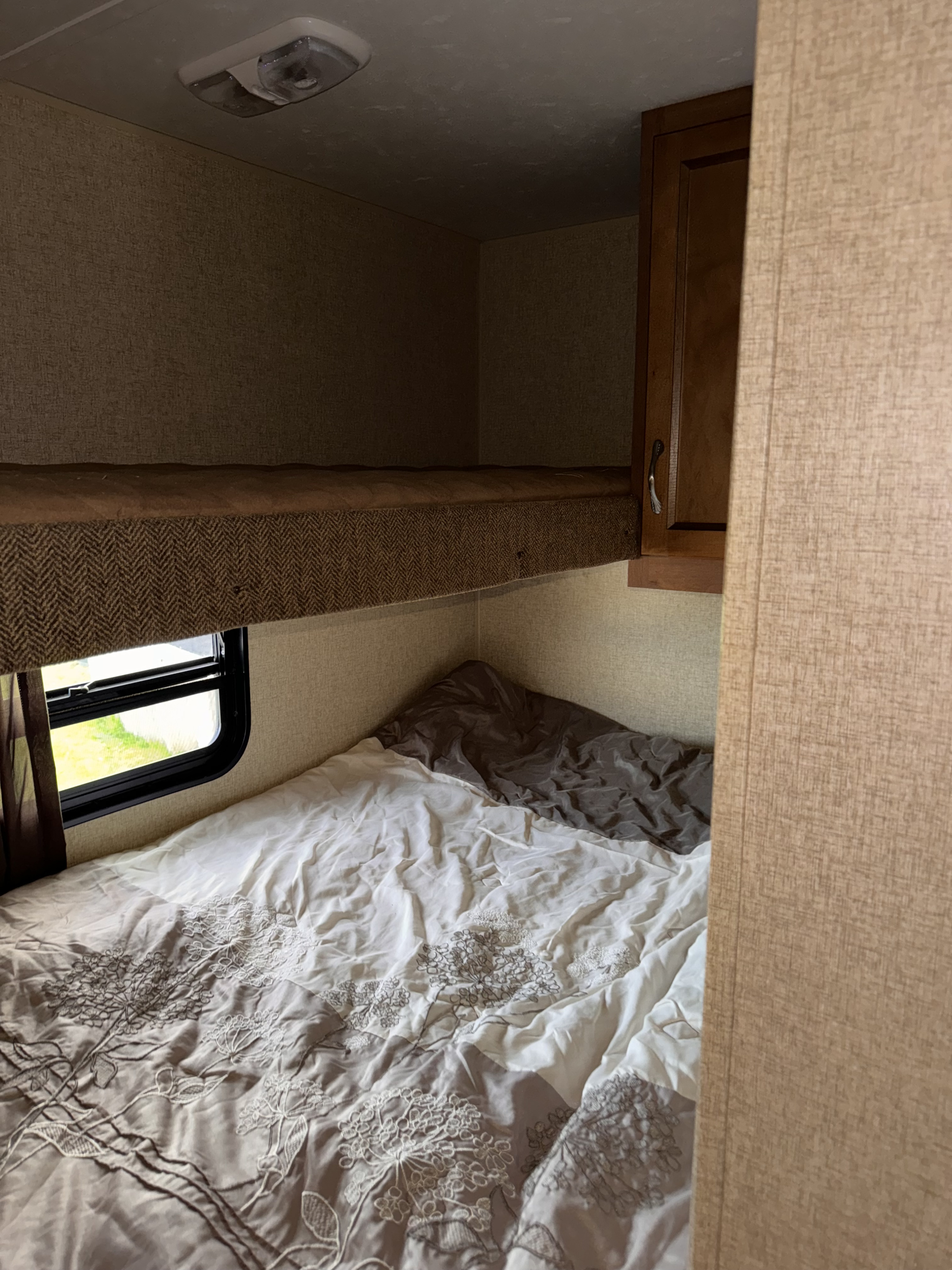 RV rental bedroom: a lower bunk with white floral bedding, an empty upper bunk, and a wooden cabinet. Ready for travel.. Coachmen Catalina 2015