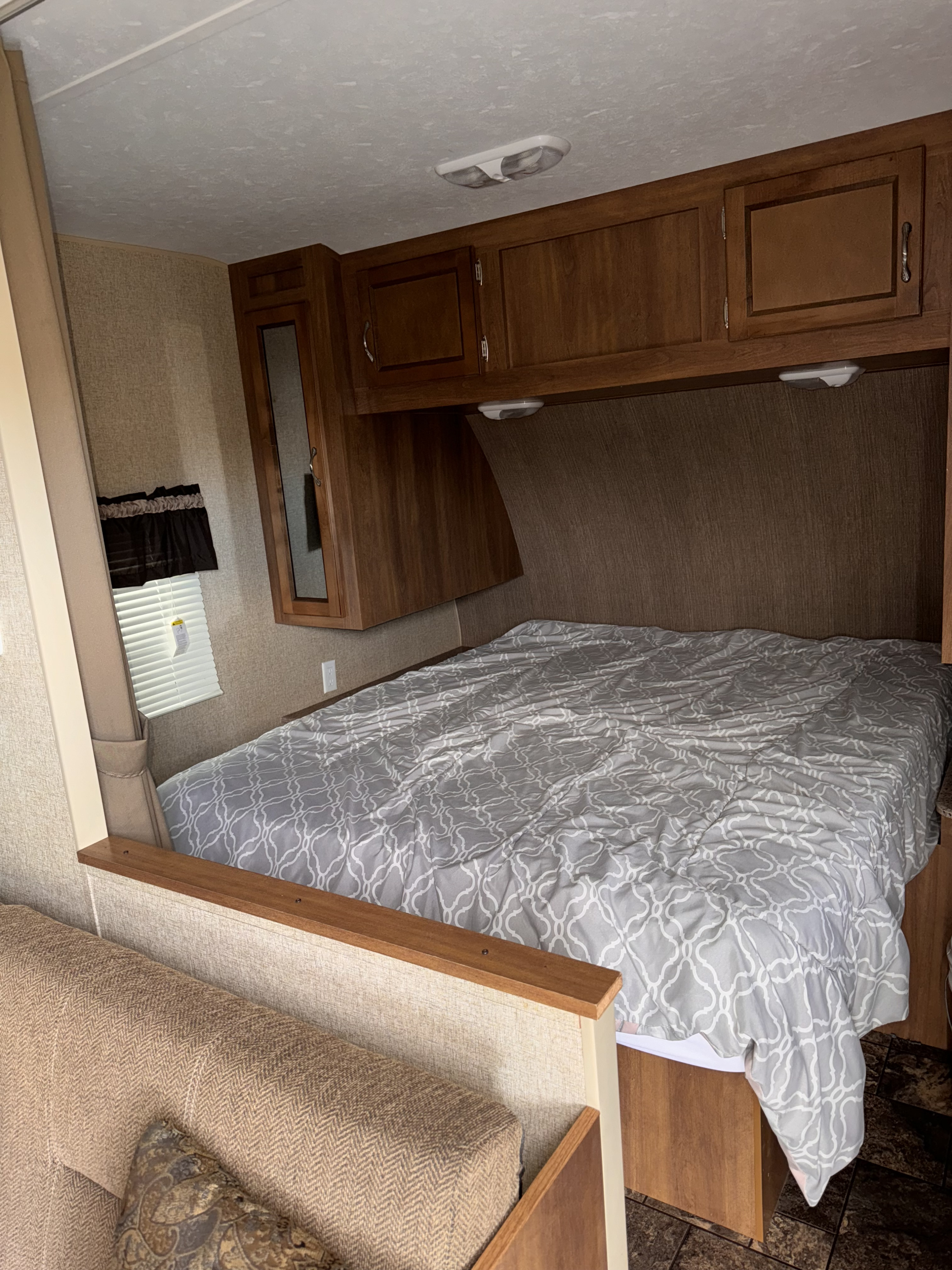 Cozy RV rental bedroom with grey patterned bed, wooden cabinets, and foreground seating area.. Coachmen Catalina 2015