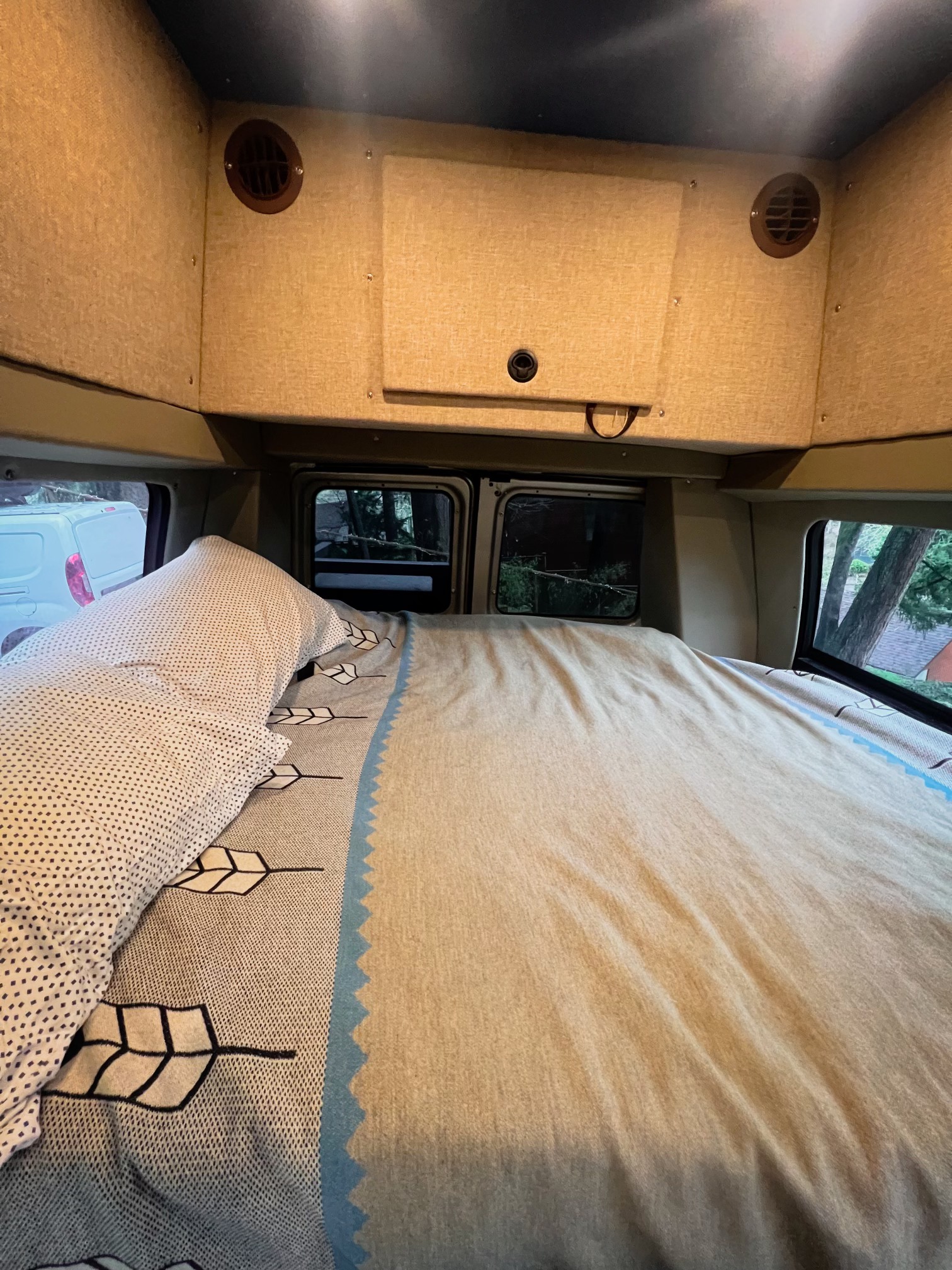An inviting RV rental interior, showing a well-made bed with patterned bedding, overhead vents, and rear windows.. Ford Econoline 150 2010