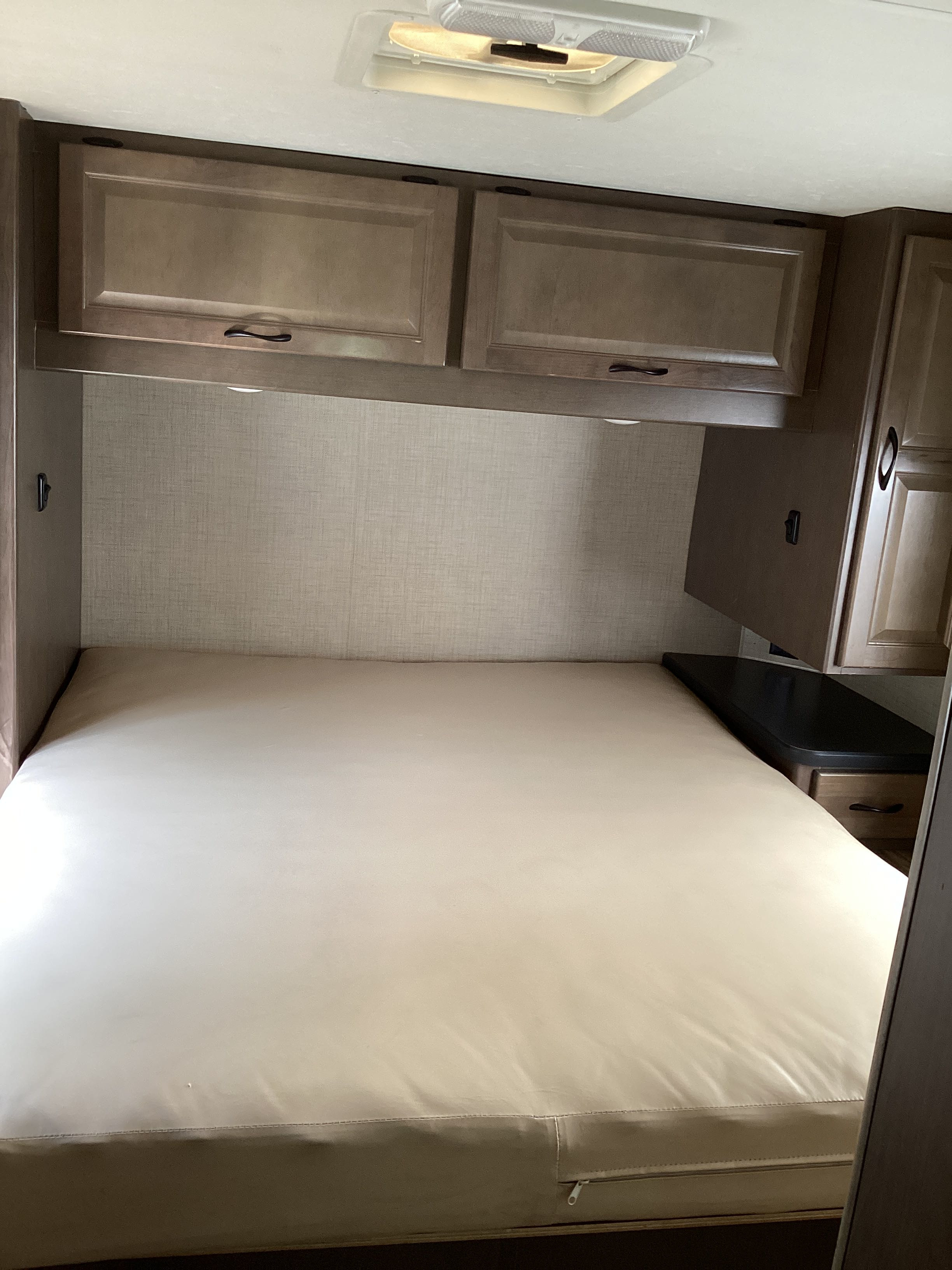 RV rental bedroom: a cozy space featuring a large mattress, overhead wood cabinets, and a convenient bedside counter.. Thor Majestic 2019