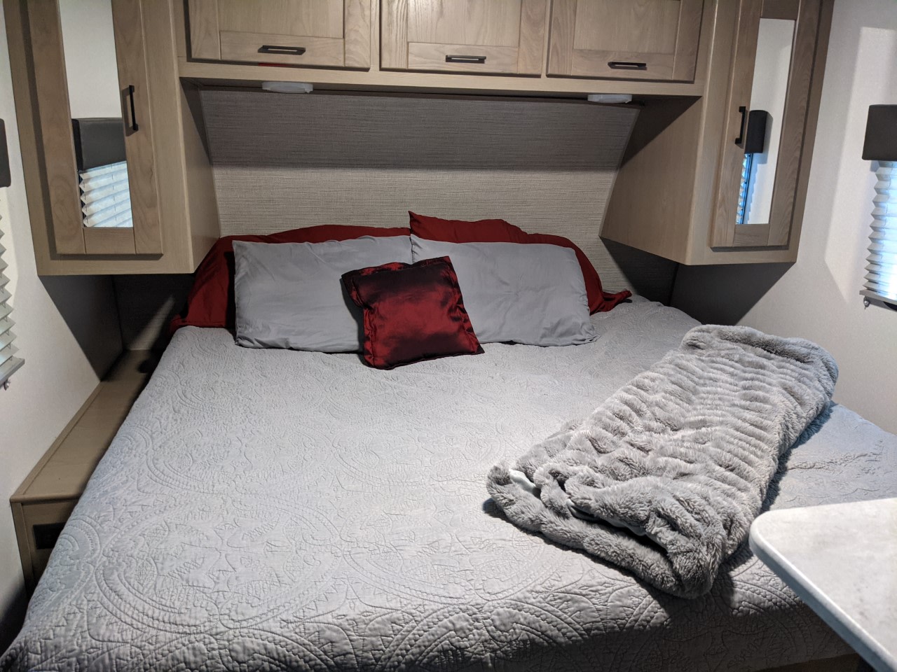 Inside an RV rental: a cozy bedroom with a neatly made bed, grey quilt, red and grey pillows, and overhead cabinets.. Cruiser RV Shadow Cruiser 2021
