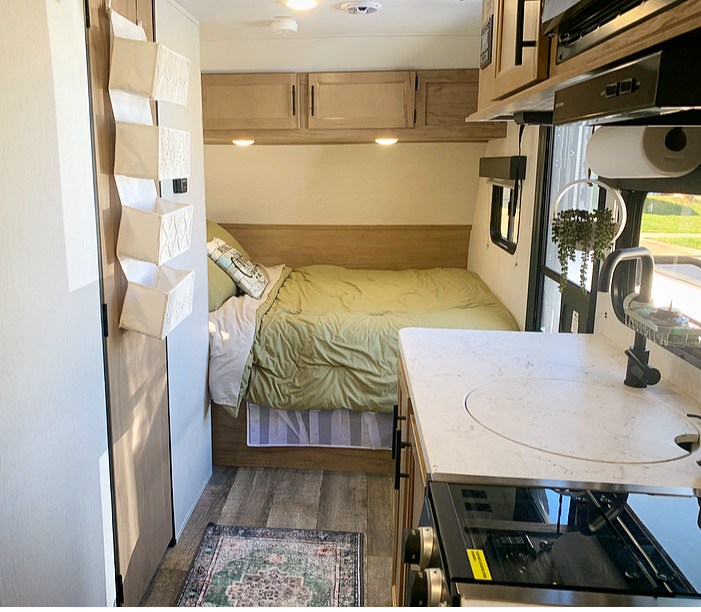 Inside a cozy RV rental: a comfortable bed with green bedding, compact kitchen, and practical hanging storage.. Forest River Cherokee Wolf Pup 2022