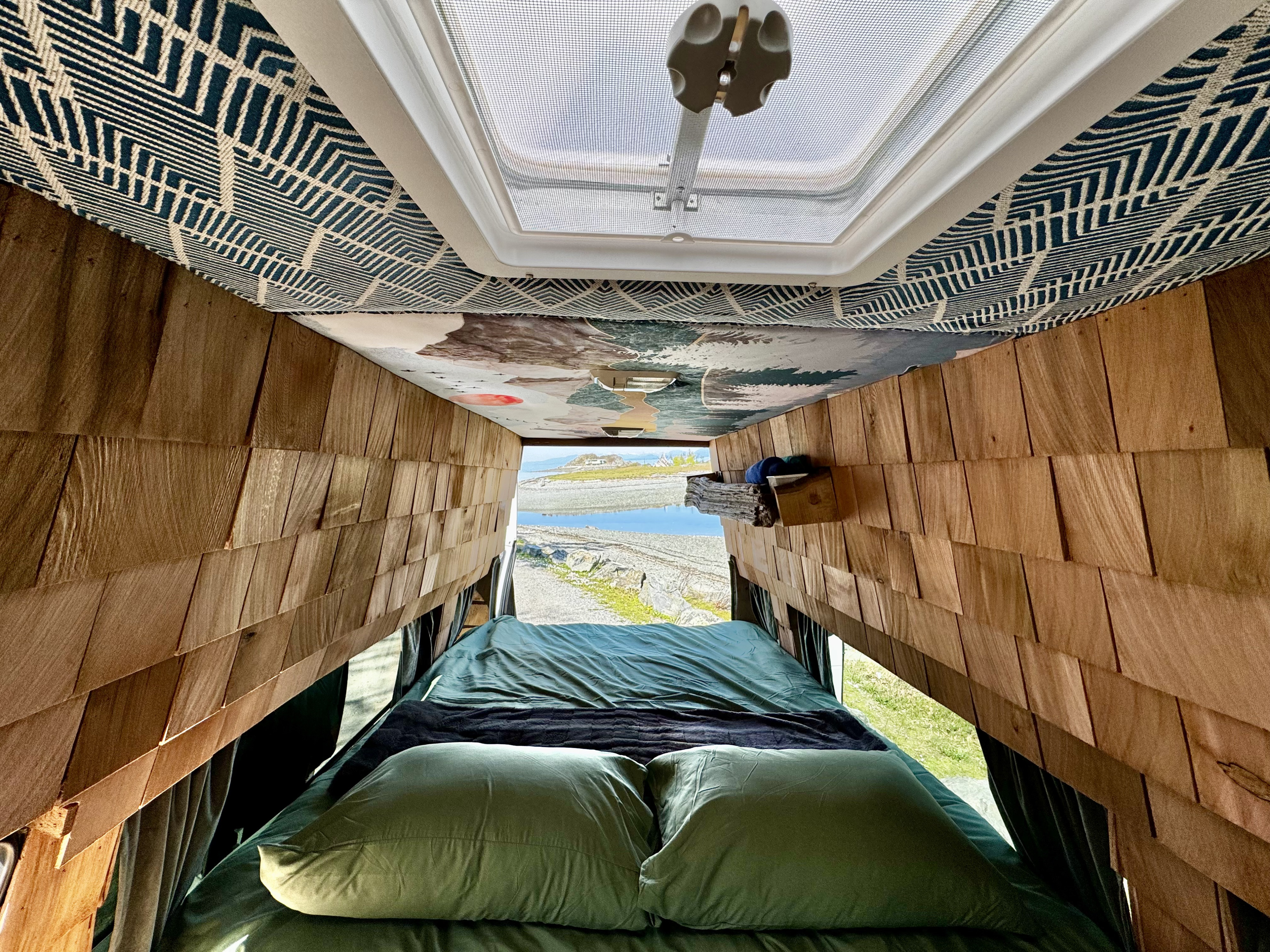 Inside a stylish rv rental: A comfy bed faces open doors revealing a serene coastal landscape. Features wood walls and patterned ceiling.. Ford Econoline E250supercab 2001