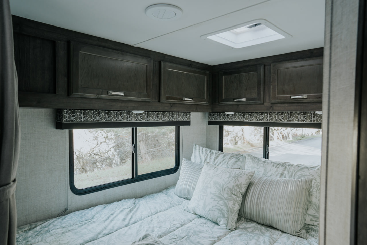 Inside a spacious RV rental bedroom featuring a comfortable bed, dark wood overhead cabinets, and large scenic windows.. Gulf Stream Conquest 2023