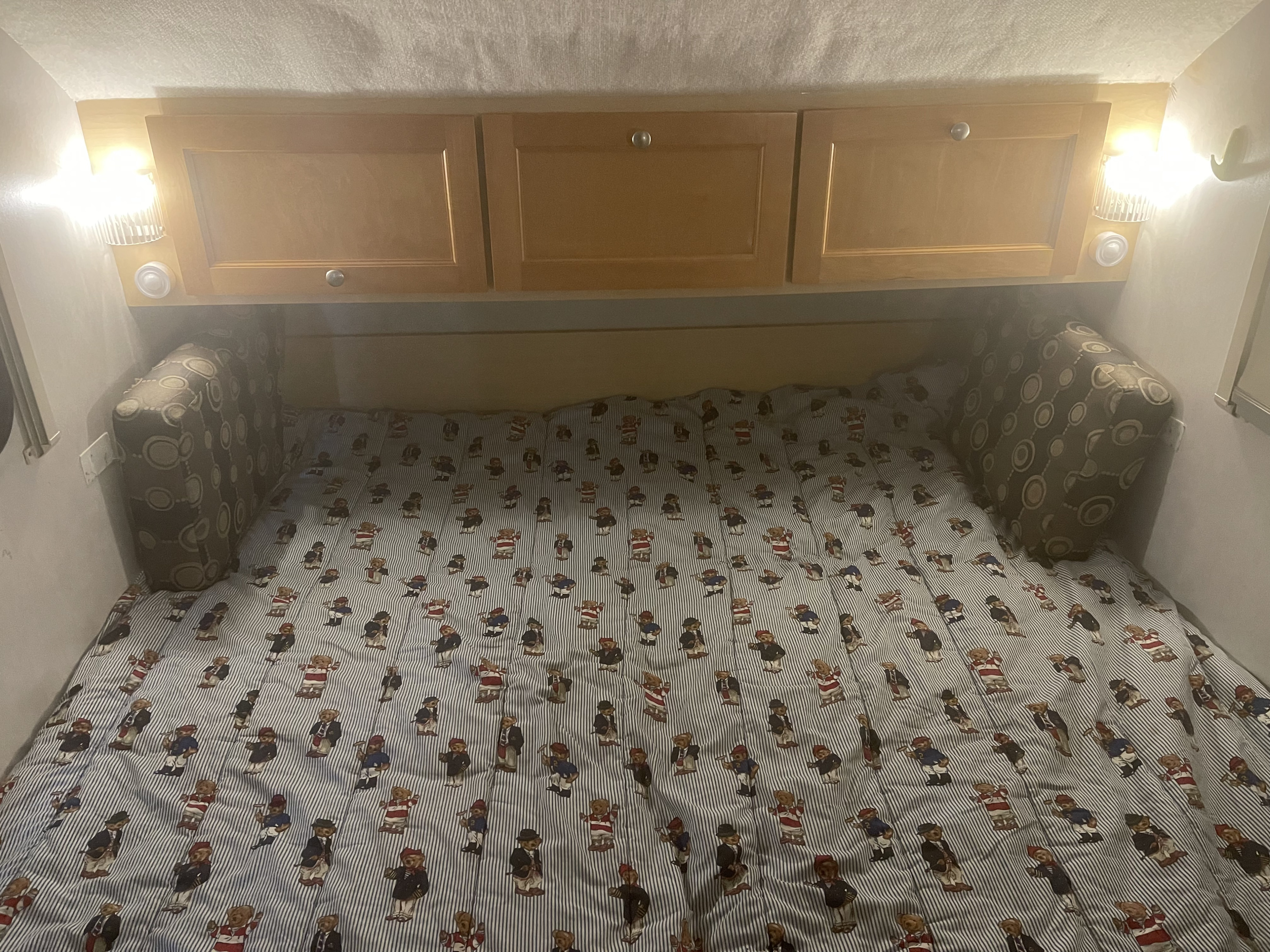 Inside an RV rental: a cozy bed with teddy bear striped comforter, overhead cabinets, and reading lights.. Thor T@b 2010