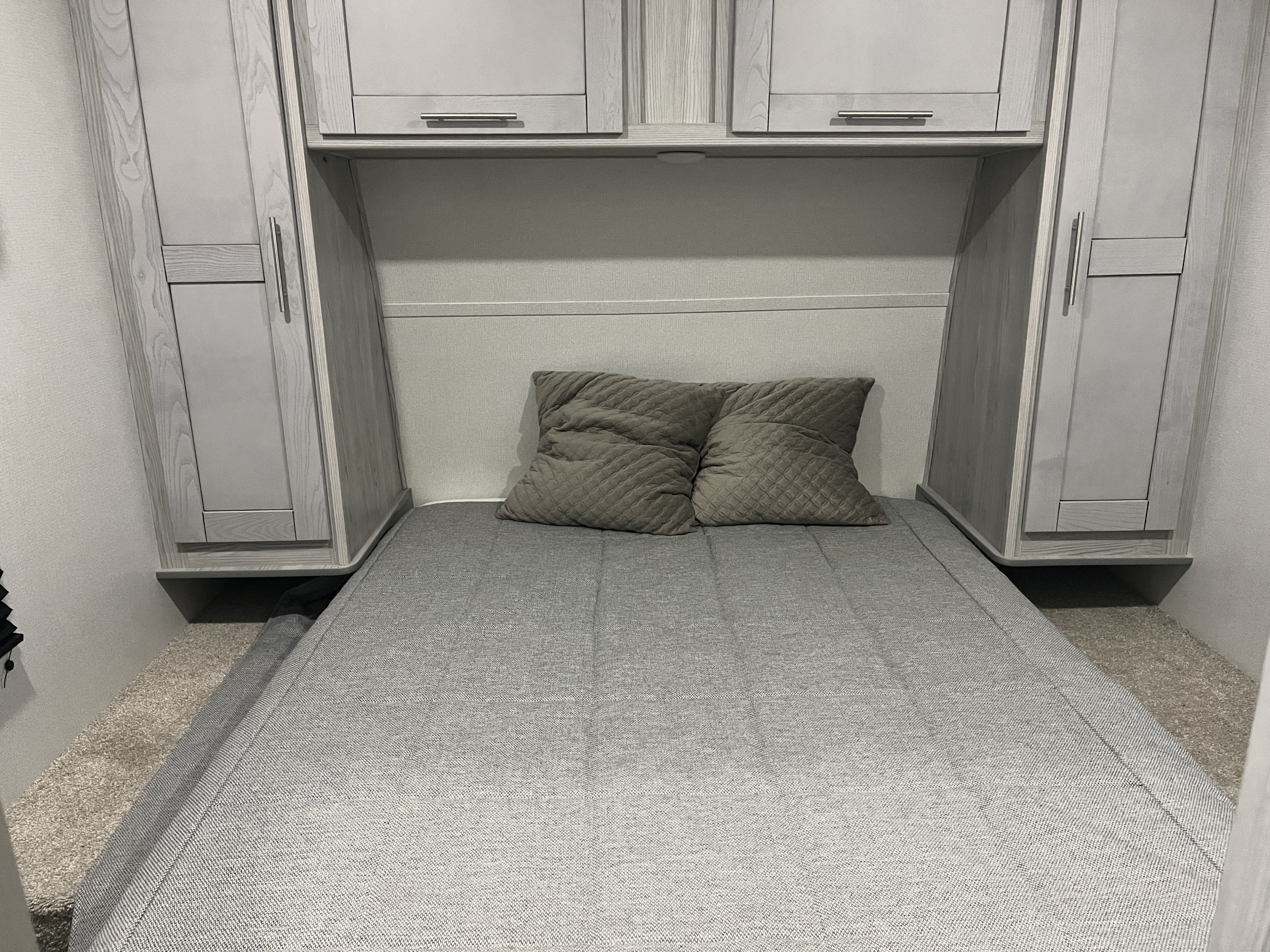 Compact grey RV rental bedroom featuring a bed with quilted pillows and light wood-grain storage cabinets.. Keystone RV Fuzion Impact Toy Hauler 2022
