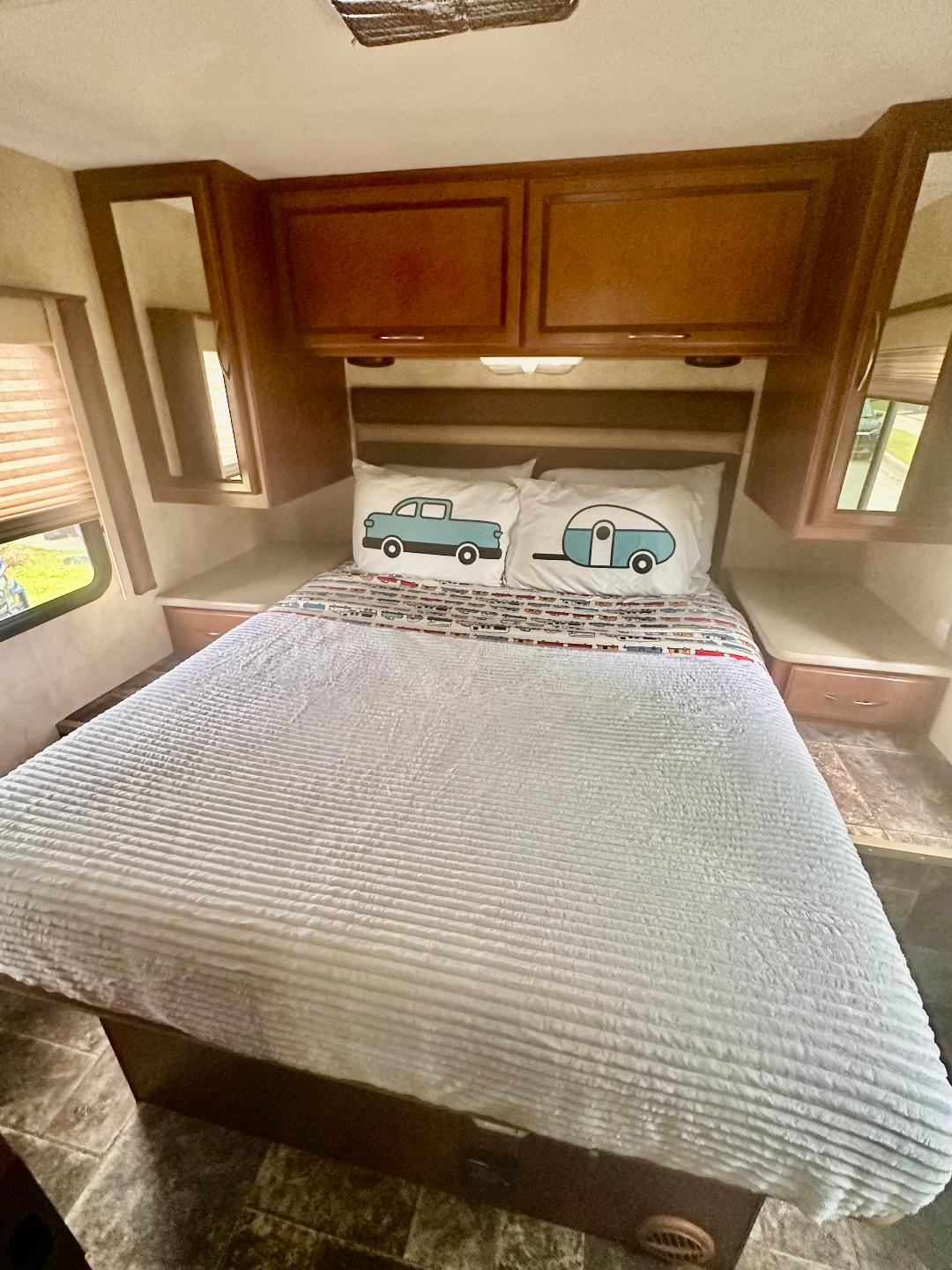 Comfortable RV rental bedroom showcasing a queen bed with unique truck and travel trailer pillows, overhead cabinetry, and side tables.. A.C.E. A.C.E. Motorhome 2014