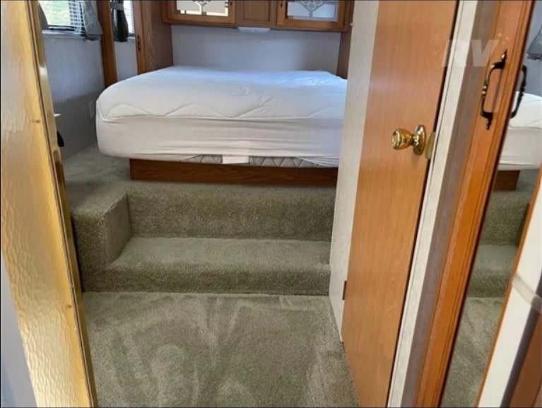 Compact RV bedroom for your rv rental: features a raised bed accessible by two carpeted steps, optimizing space.. K-Z Manufacturing Sportsmen 2003