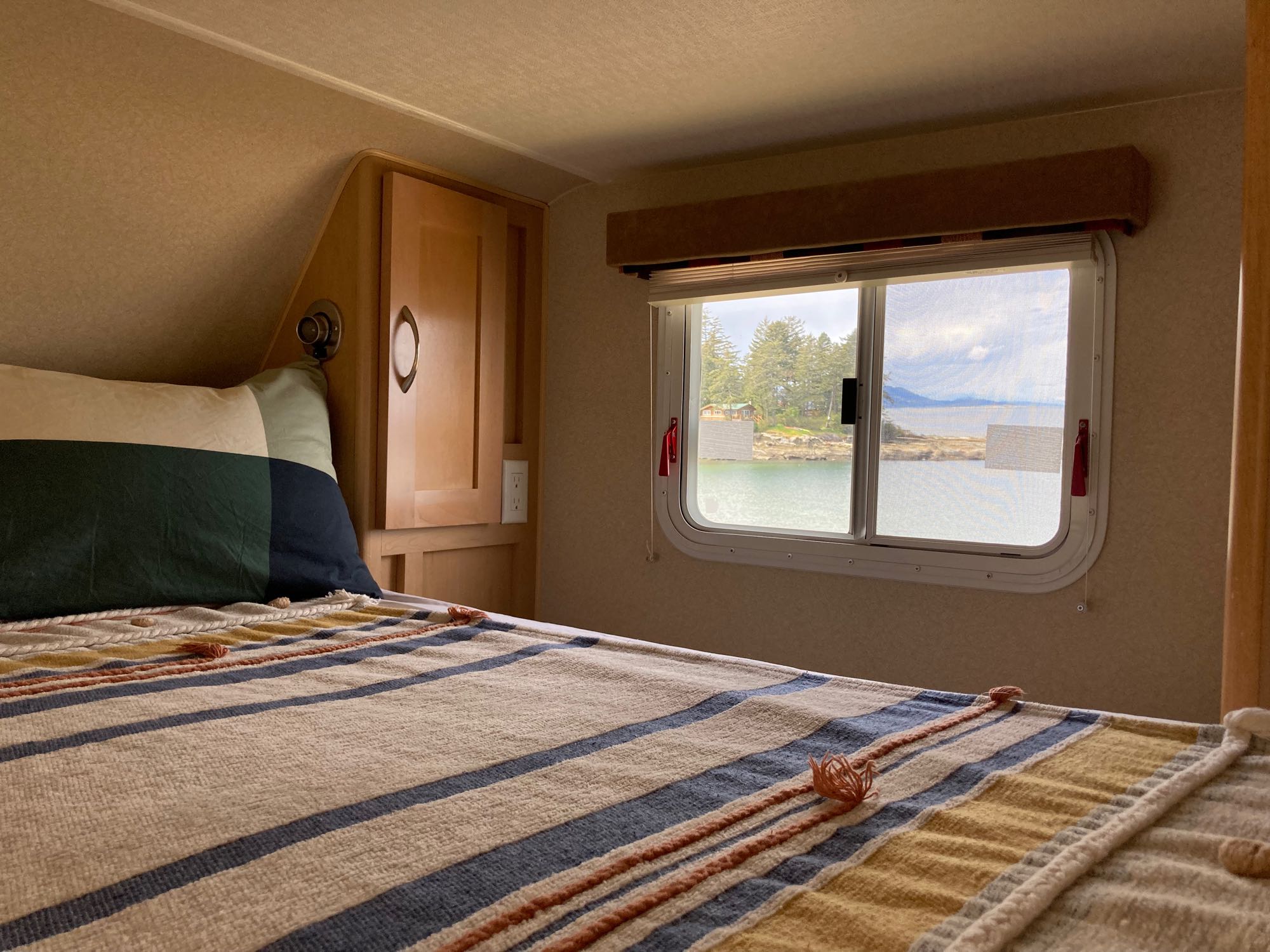 Cozy RV rental interior with a bed and a stunning window view of a serene bay and forested islands. Ideal for travel.. Chevrolet Other 2010