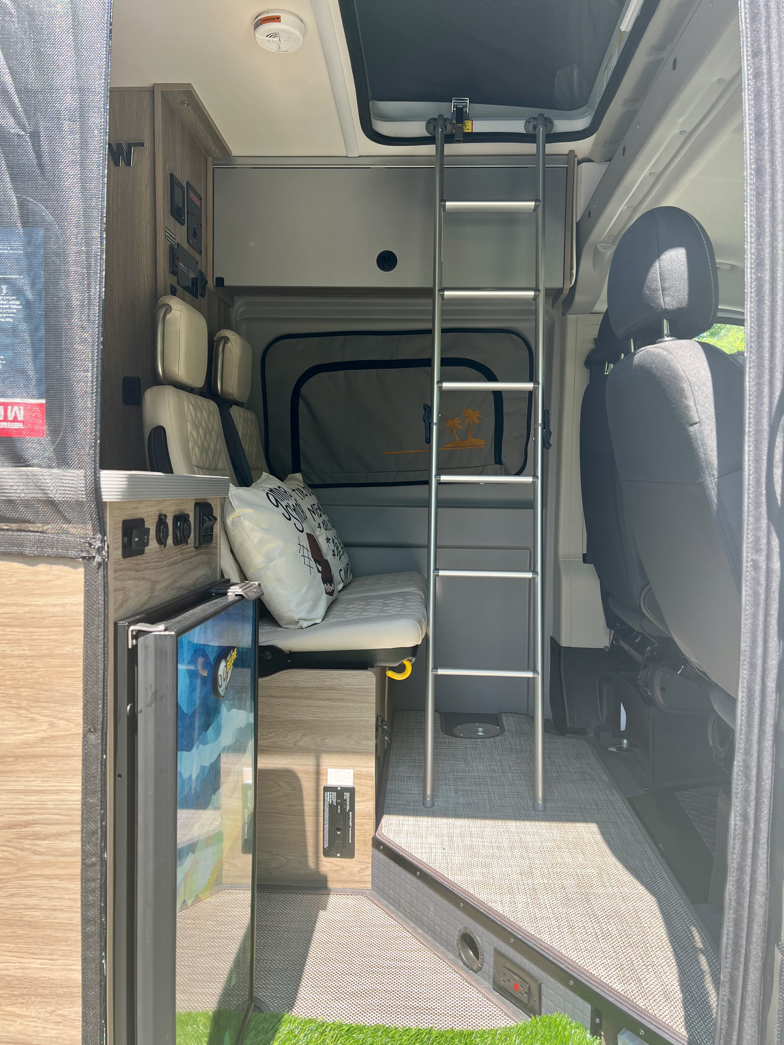 View inside a modern RV rental featuring a bunk bed, bench seating, compact fridge, and control panel for road trip comfort.. Winnebago Solis 2024