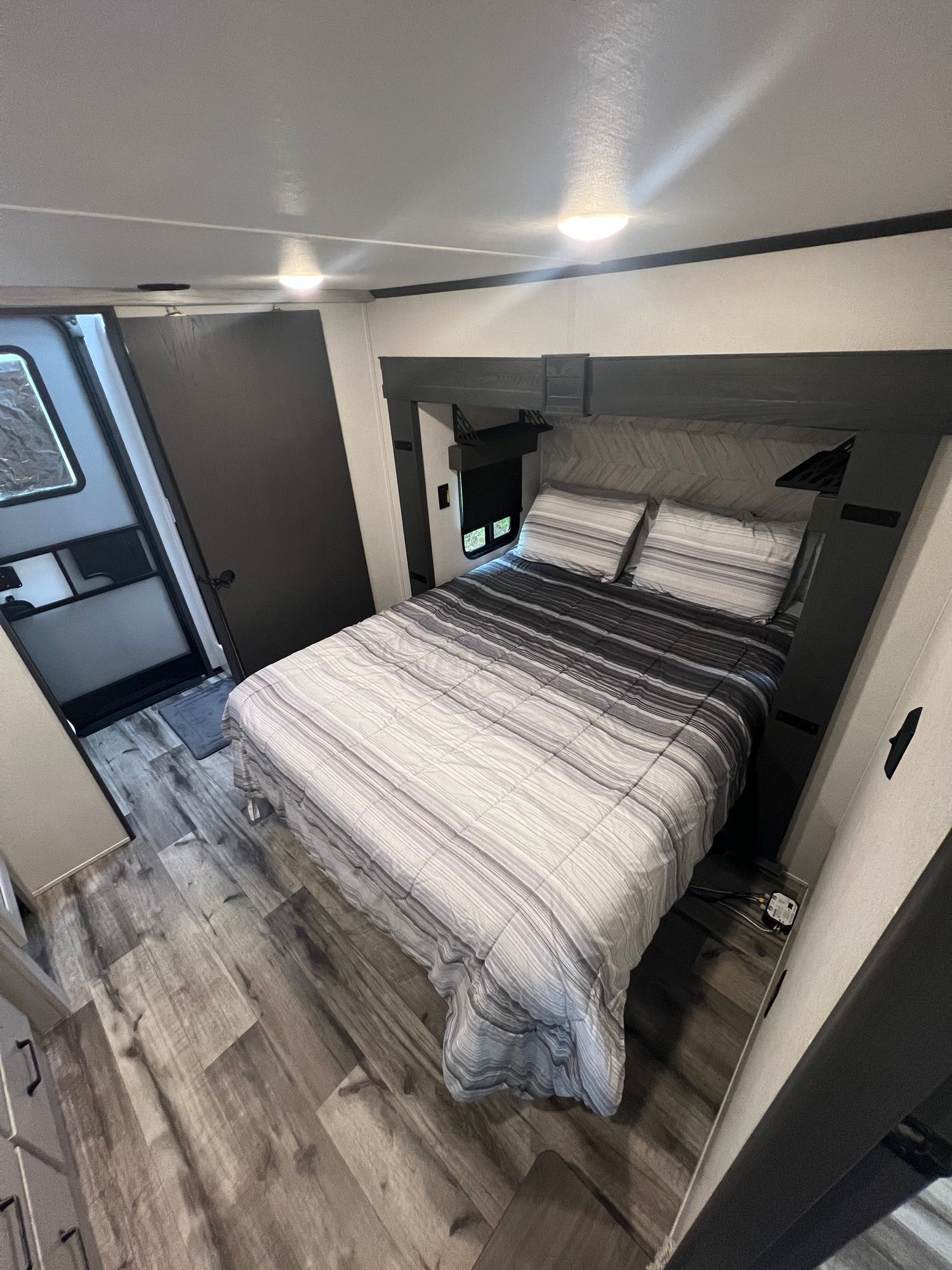 Explore this modern RV rental bedroom featuring striped bedding, wood-look flooring, and ample storage. Comfortable and functional.. Keystone RV Montana High Country 2023