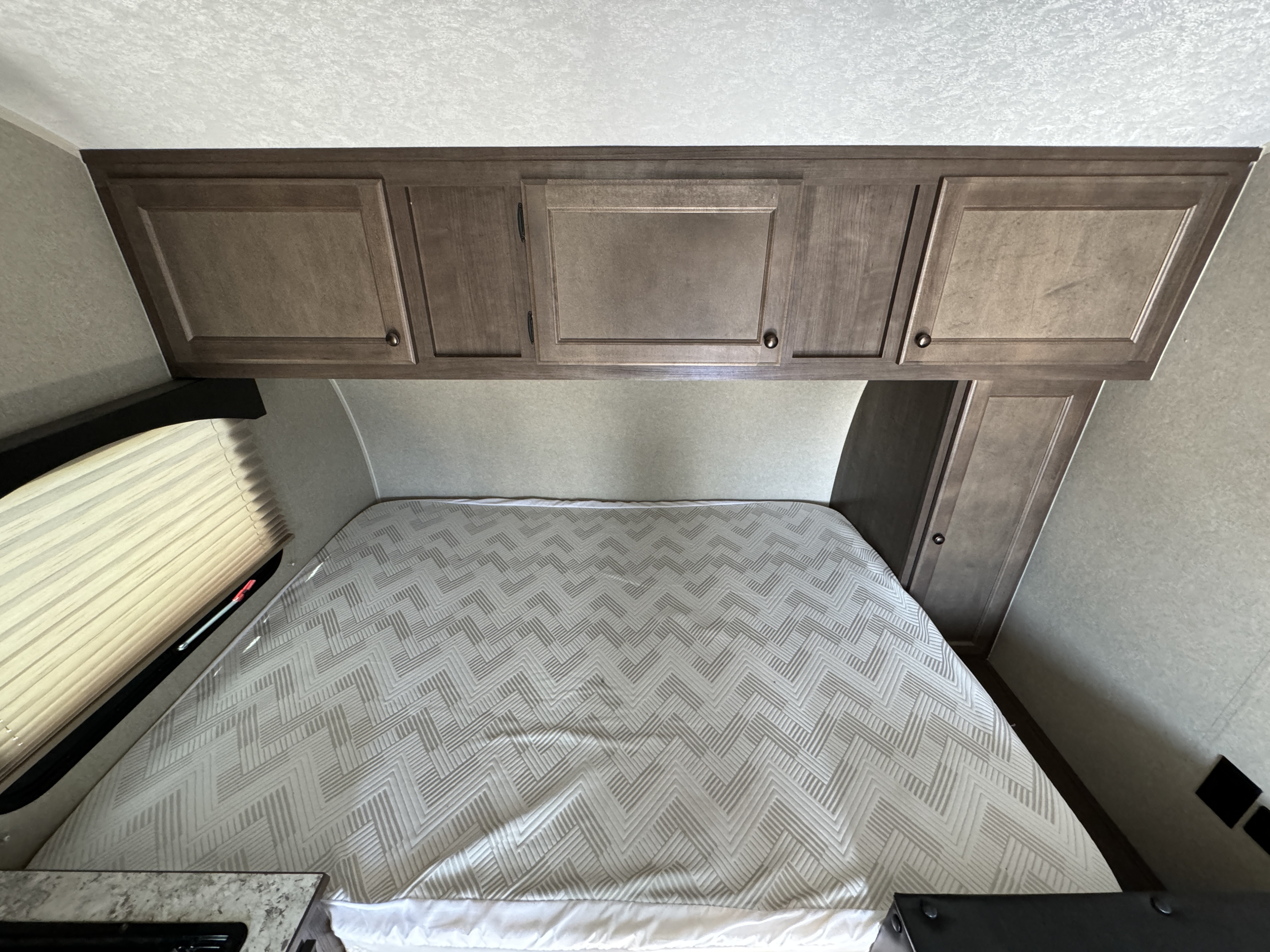 RV rental bedroom: Overhead cabinets, a bed with a chevron pattern, and window blinds in a compact space.. Sun Lite 16BH Classic 2021