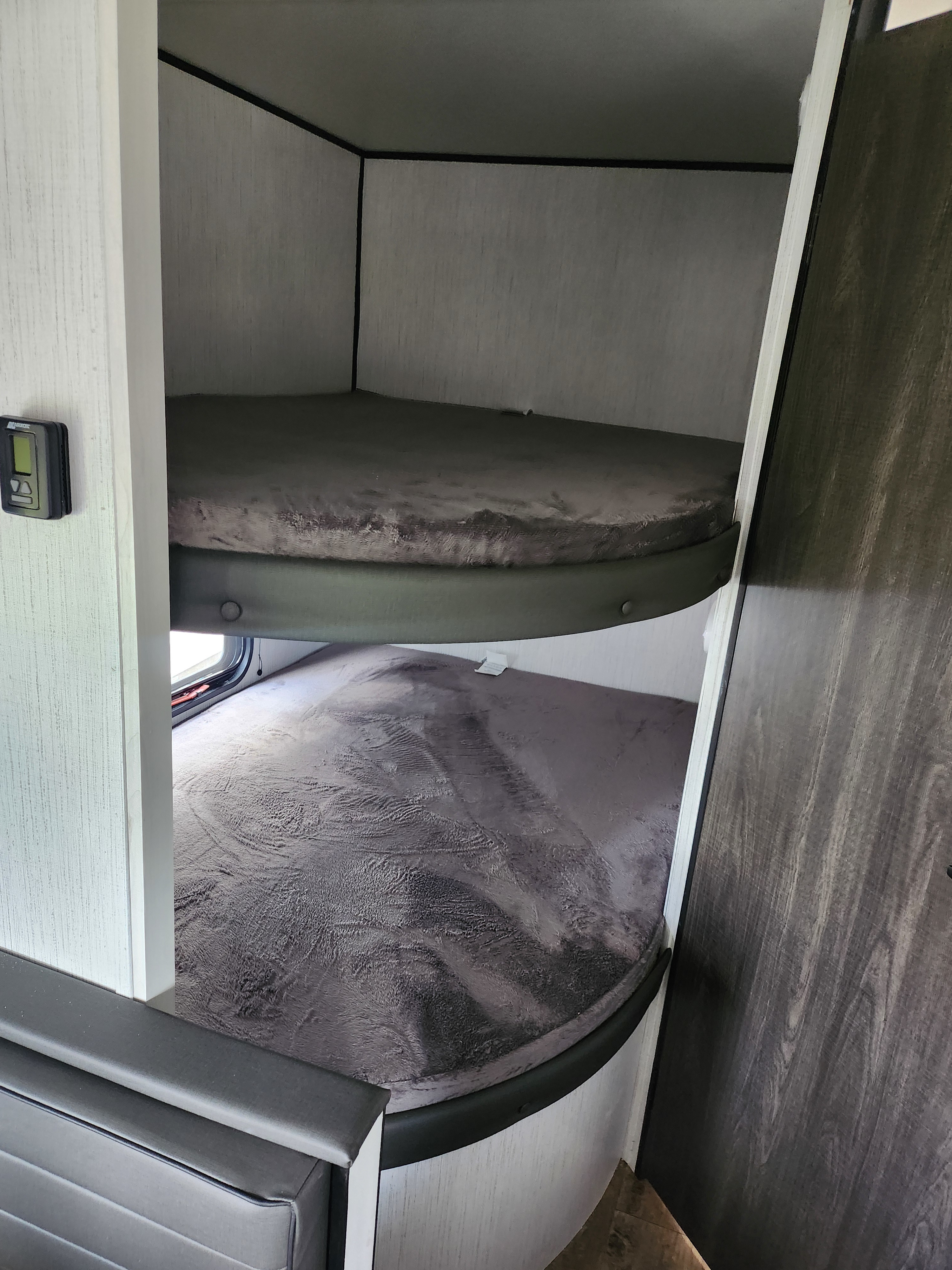 Cozy RV rental bunk beds with soft gray blankets, control panel, and window in modern RV interior.. Heartland RVs Trail Runner 2022