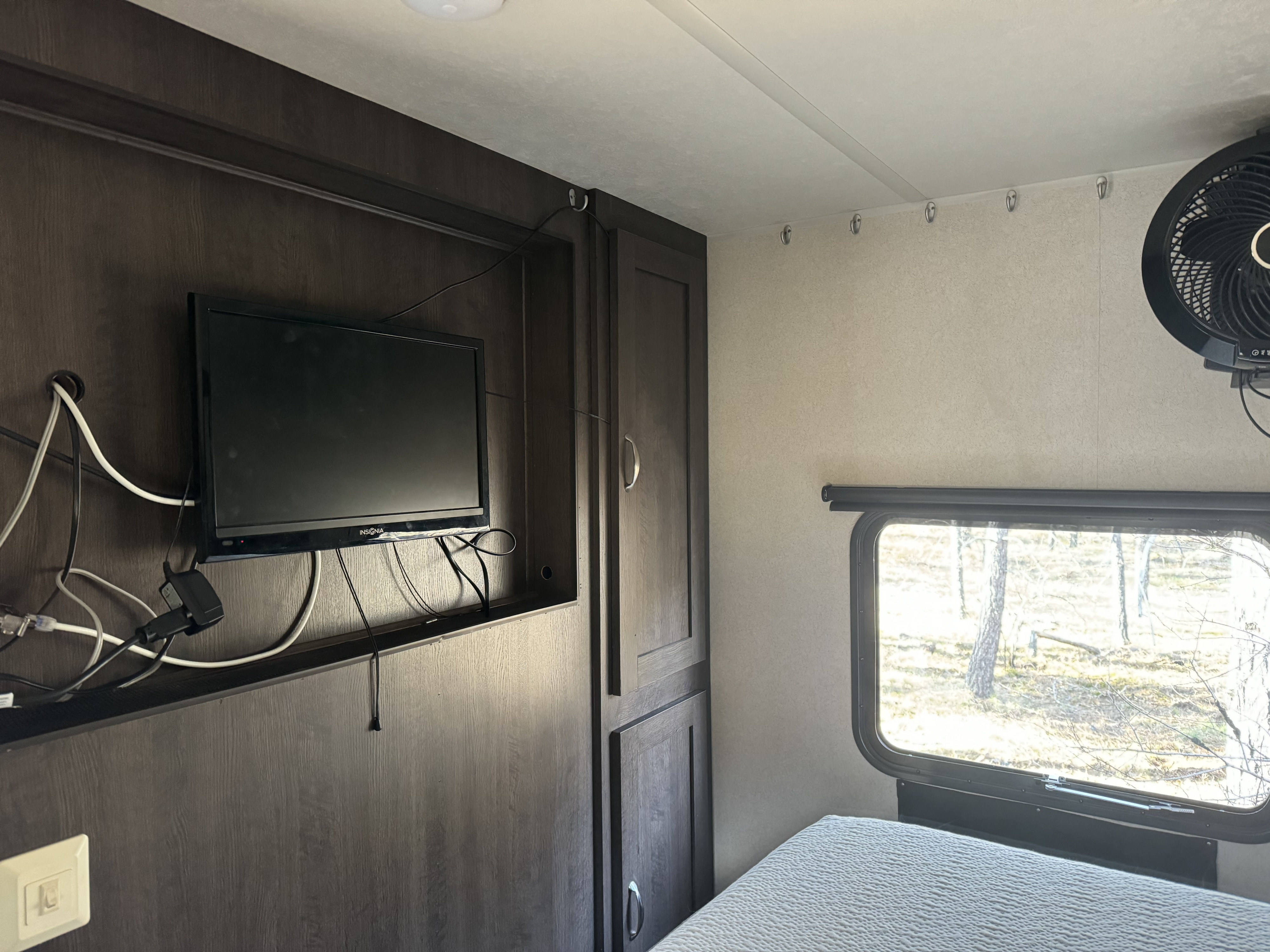 Cozy RV rental bedroom with TV, window view of forest, and overhead hooks. Perfect for a nature getaway.. Forest River Wild wood 2017