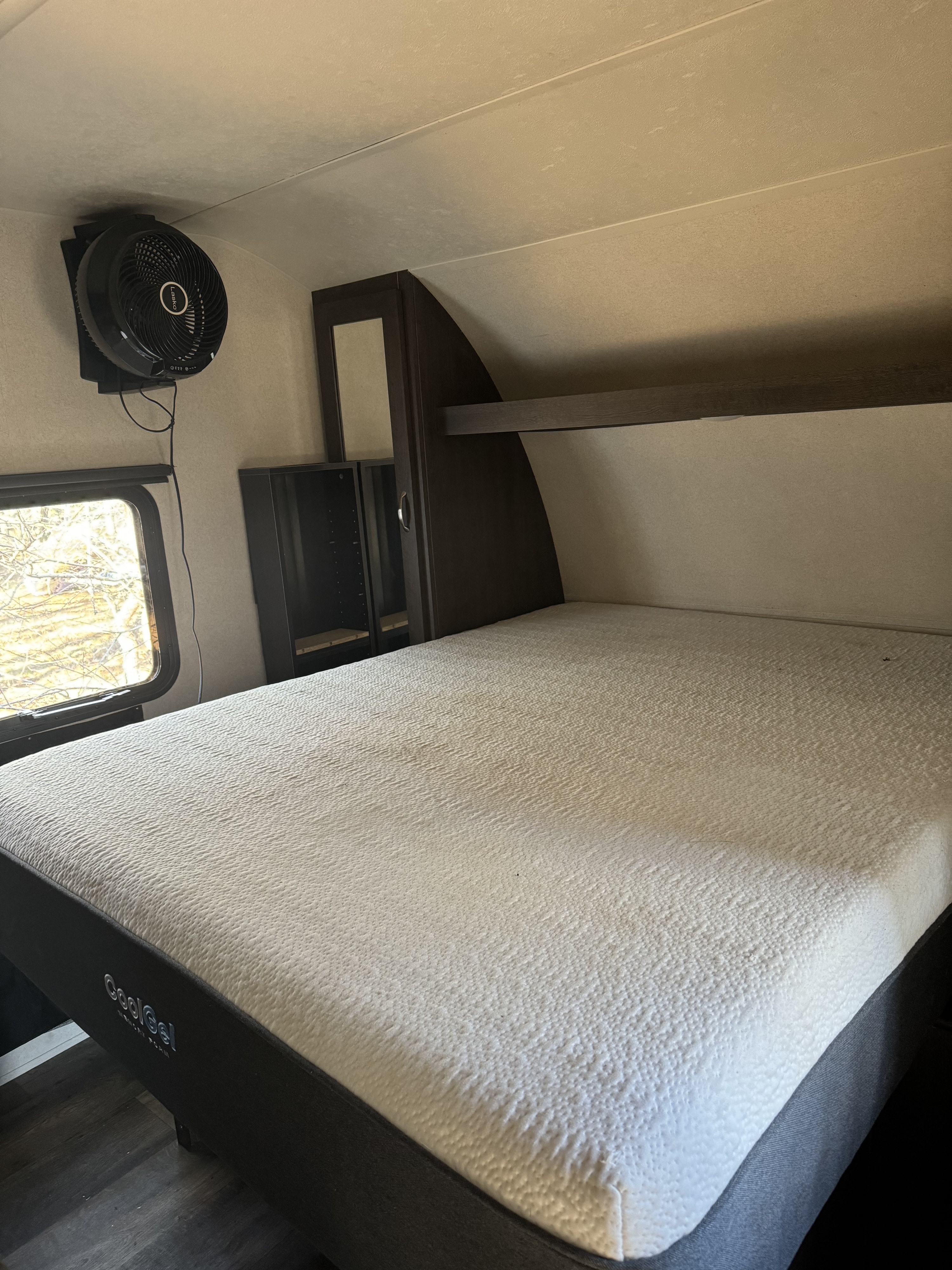 RV rental bedroom with a CoolGel mattress, wall-mounted Lasko fan, dark storage, and window.. Forest River Wild wood 2017